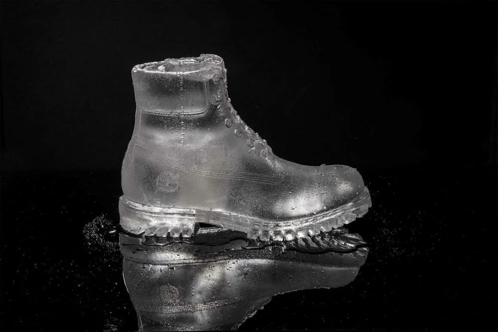 A transparent ice boot on a reflective black surface with a black background.