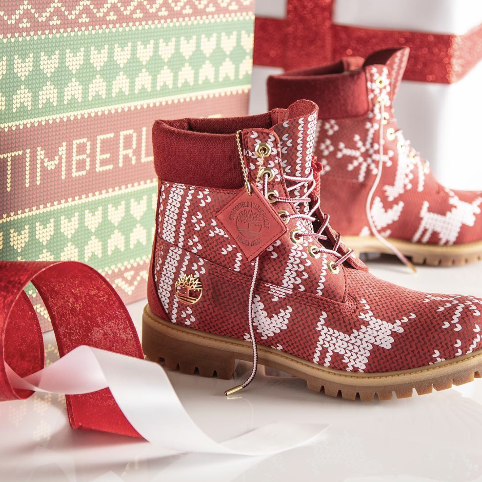 Pair of red patterned winter boots with Christmas-themed designs, surrounded by holiday gift wrap and ribbons.