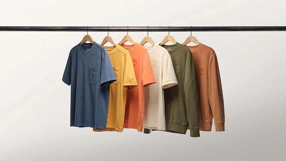 Six colorful T-shirts hanging on a black clothing rack against a white background.