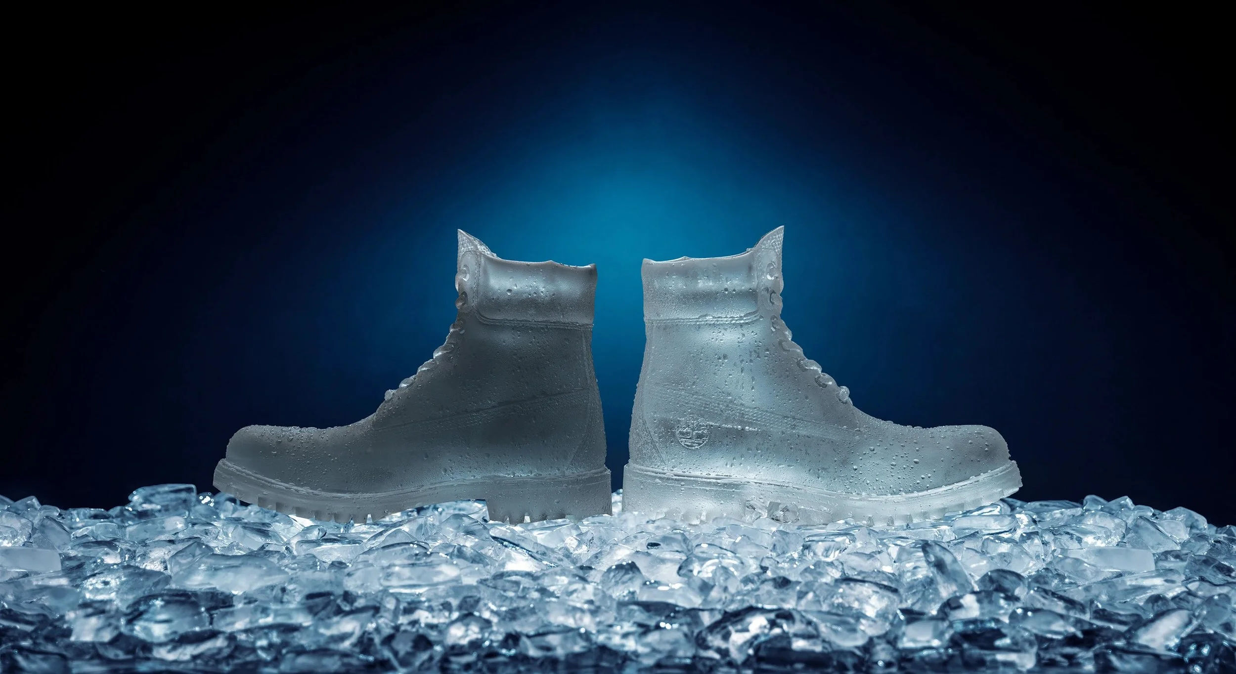 Ice boots with condensation, sitting on a bed of crushed ice, illuminated with a cool blue light.