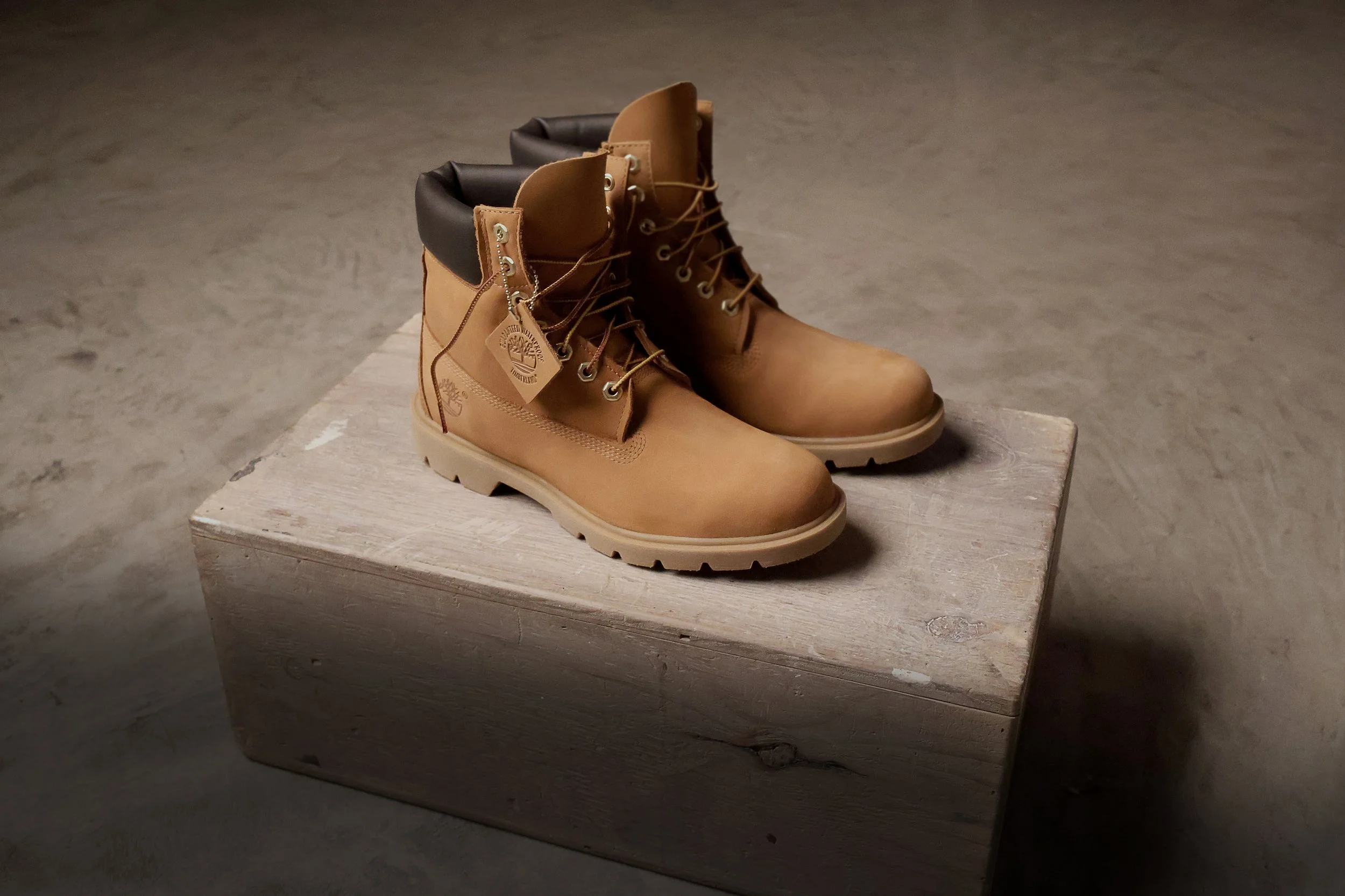 A pair of yellow Timberland work boots with black padded collars placed on a weathered wooden block.