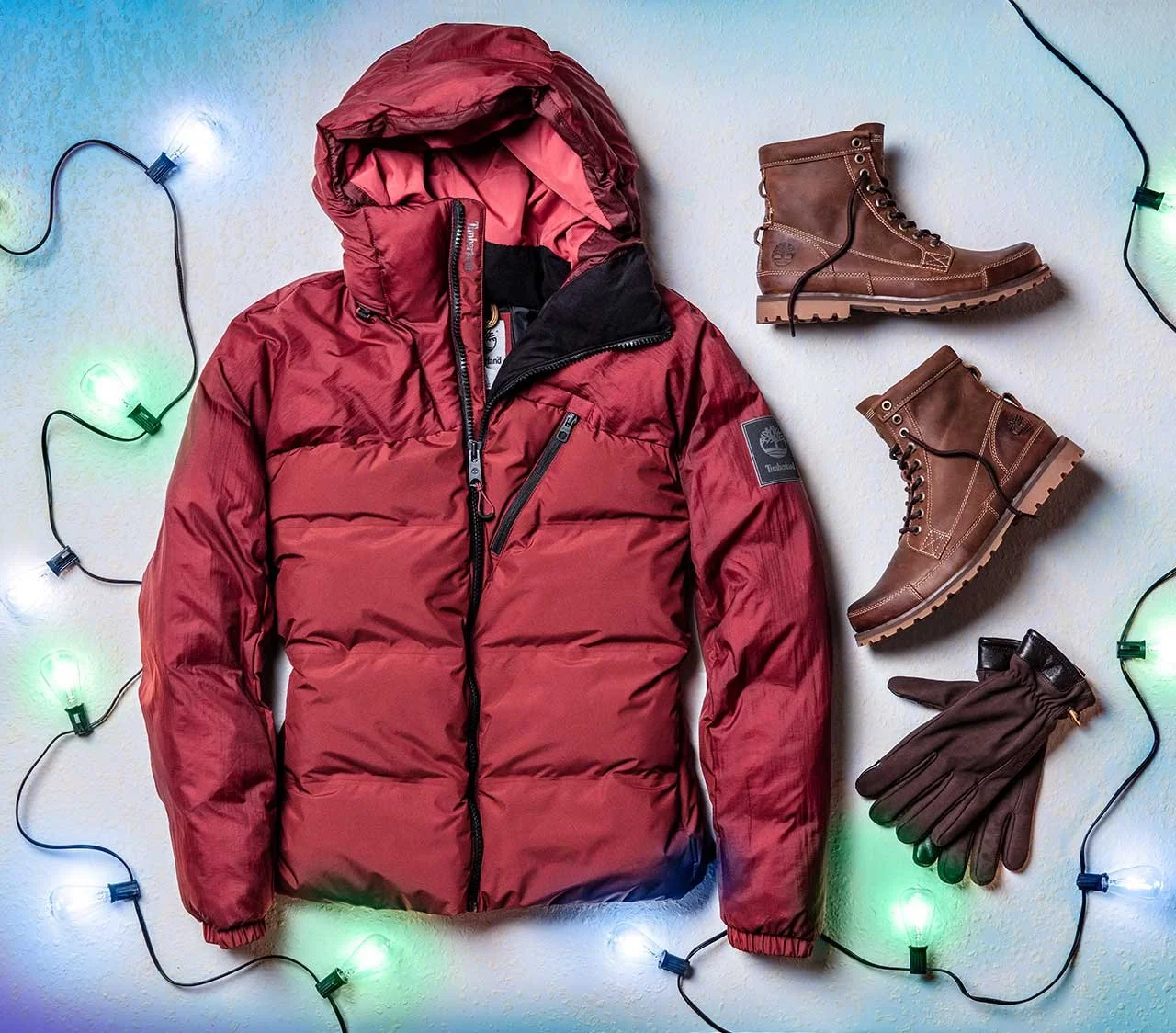 Red insulated winter jacket, brown leather hiking boots, and brown gloves surrounded by colorful string lights.