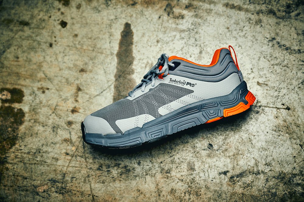 A gray and orange Timberland PRO warehouse shoe with a sturdy sole, resting on a rough concrete floor.