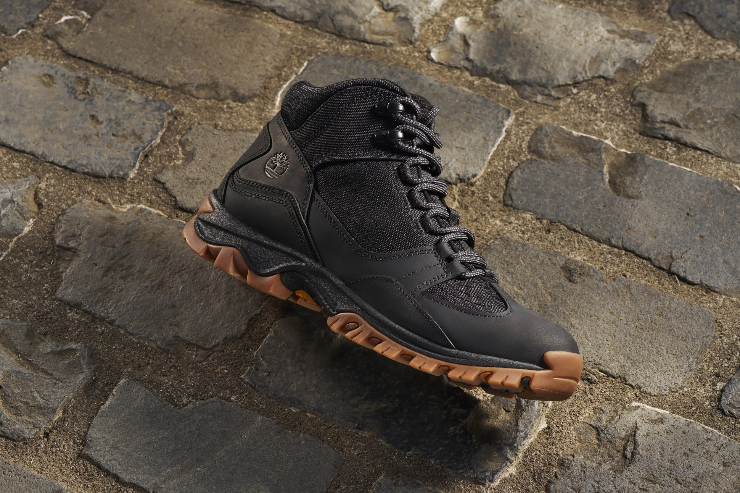 A black hiking boot with a Timberland logo on the side, resting on a cobblestone surface.