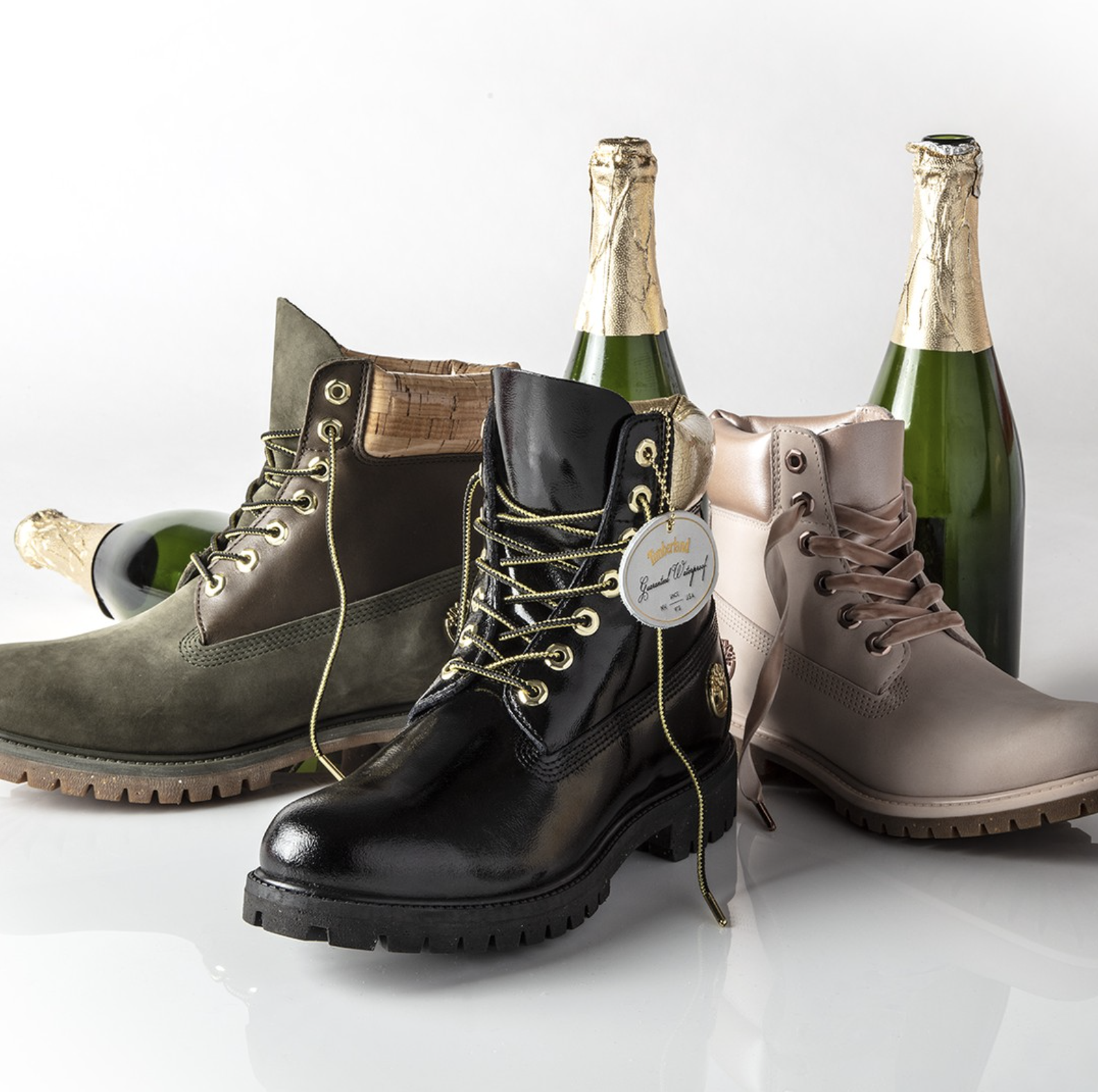Pair of brown, black, and beige boots with gold eyelets, and champagne bottles with gold foil caps against a white background.