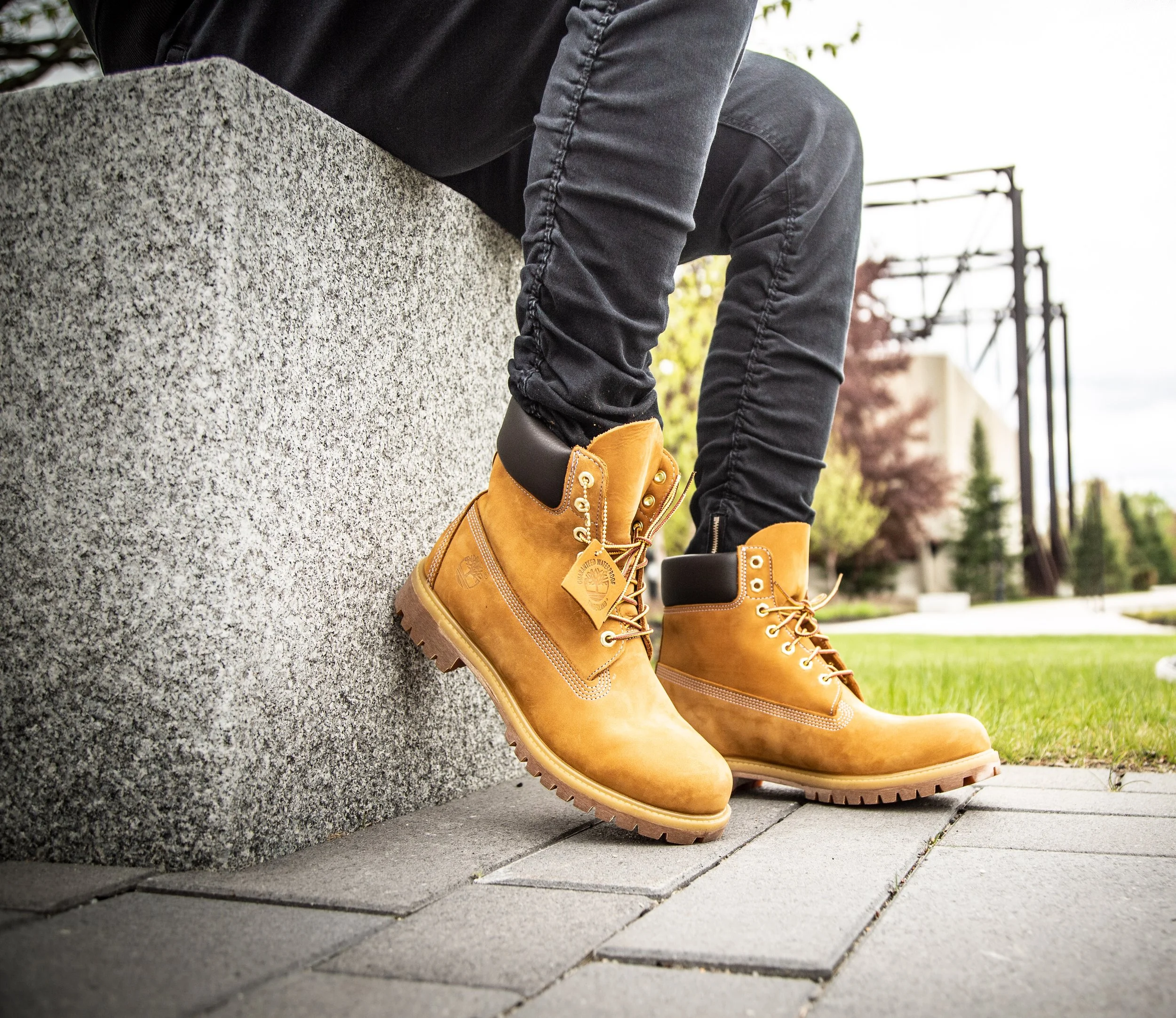 Person wearing tan Timberland boots sitting on a concrete structure outdoors.