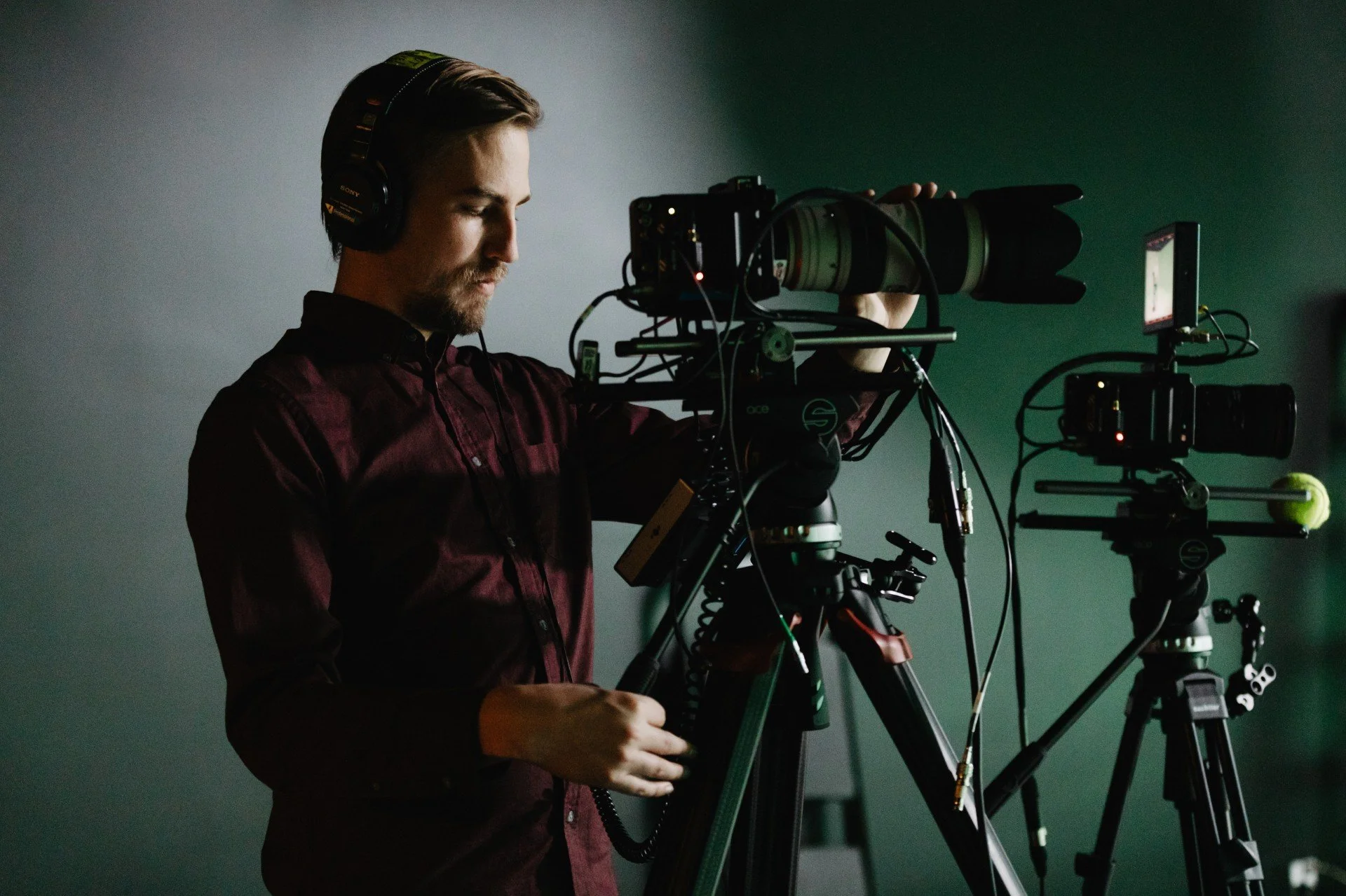 A man in a dark shirt operating professional camera equipment on tripods in a dimly lit studio.