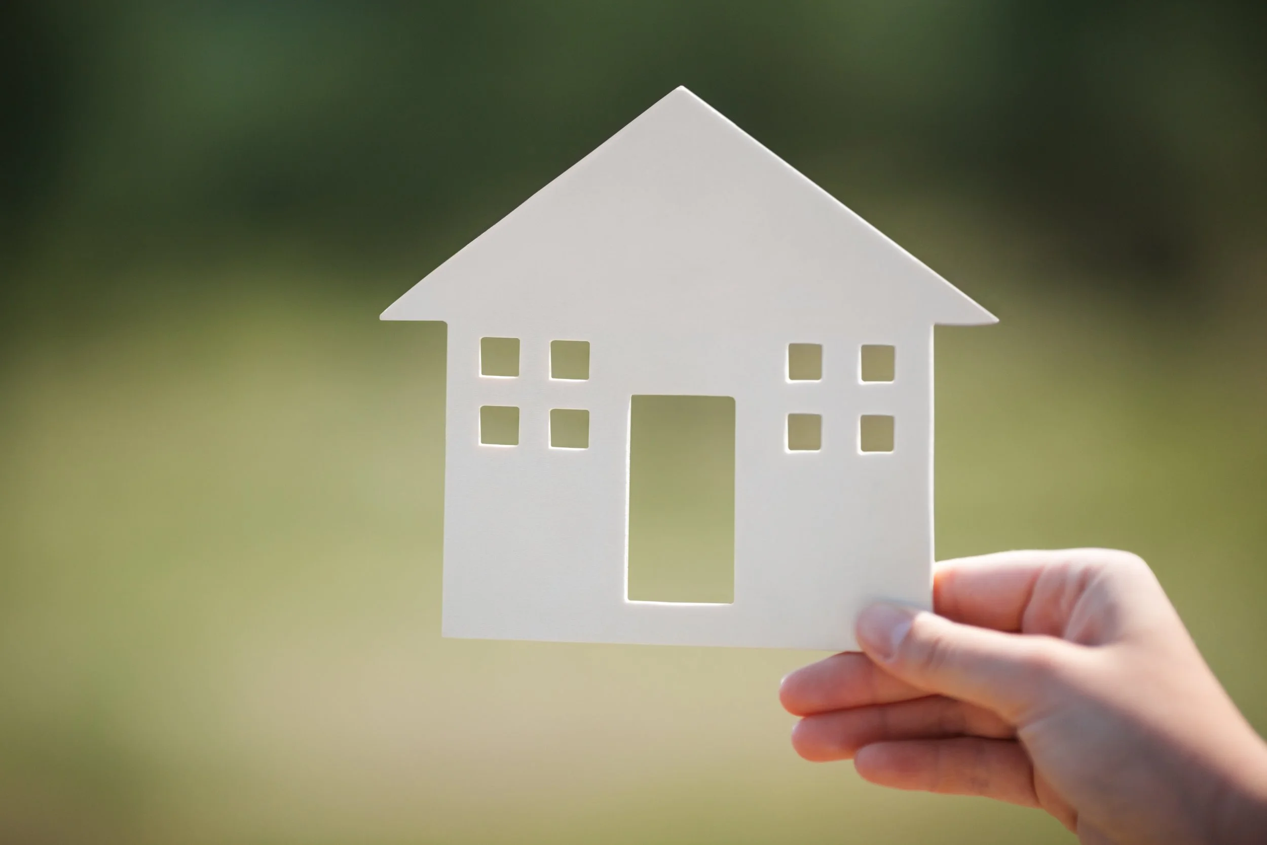 Person holding a paper cutout of a house against a blurred green background.