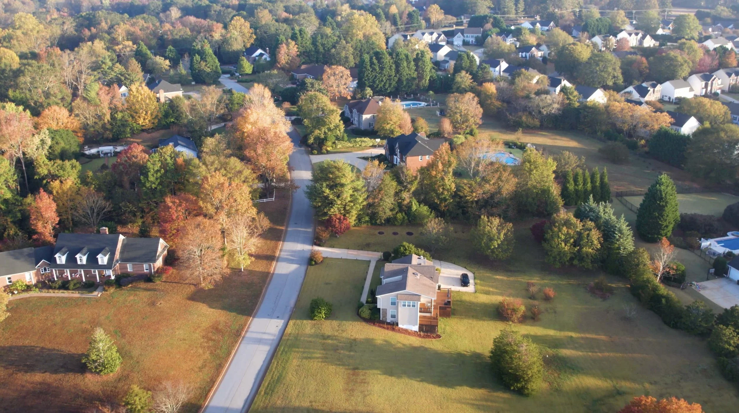 Aerial view of a suburban neighborhood with winding roads, large houses, and lots of trees with fall foliage.