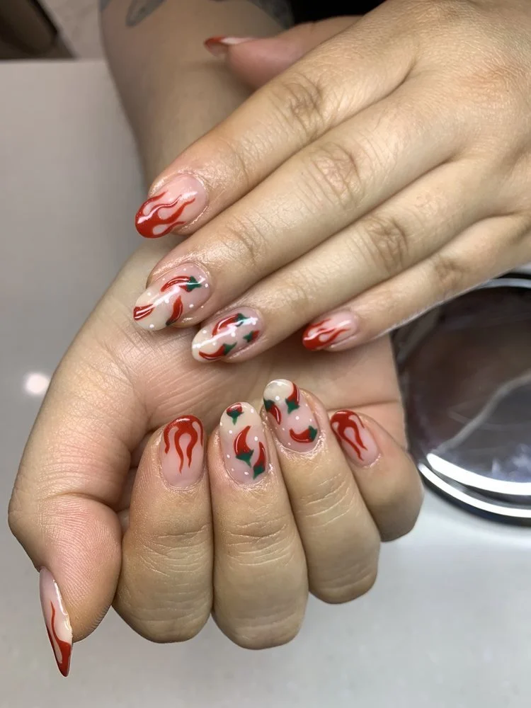 Nail art on both hands featuring red and green chili pepper designs on a nude base.