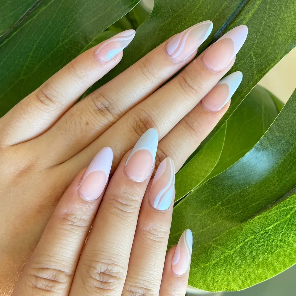 Close-up of hands with manicured nails featuring pastel pink and blue nail art, on a green leafy background.