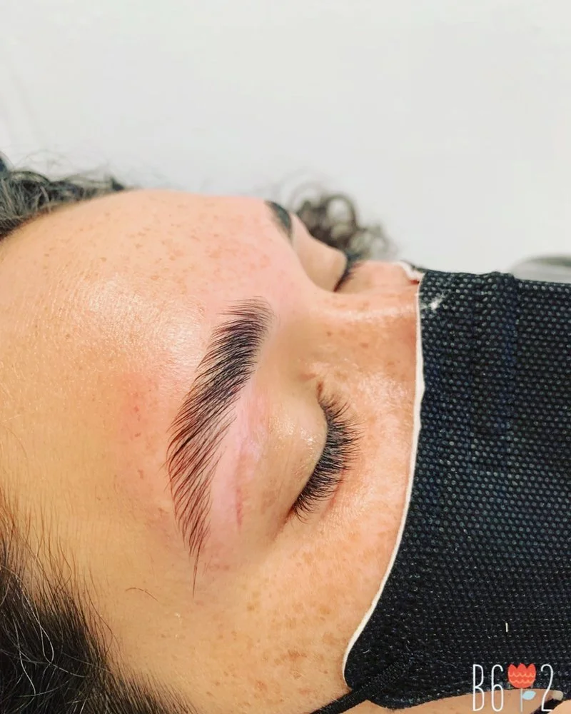 Close-up of a person's face with closed eyes, showing well-groomed eyebrows, freckles, and wearing a black face mask.