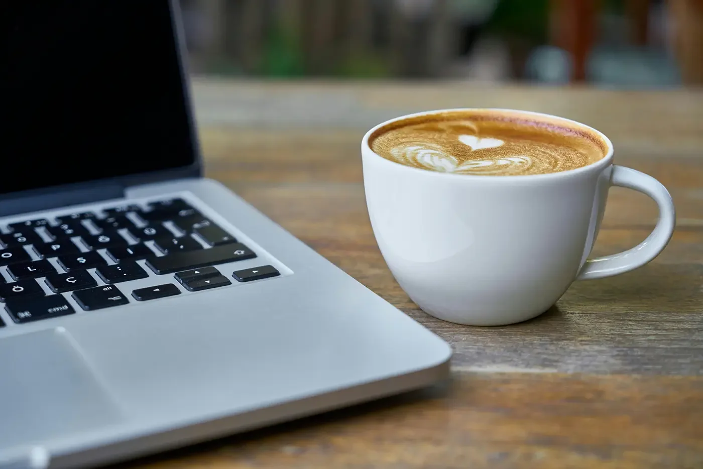 corner of a laptop an with a cup of coffee. both are on a wooden surface
