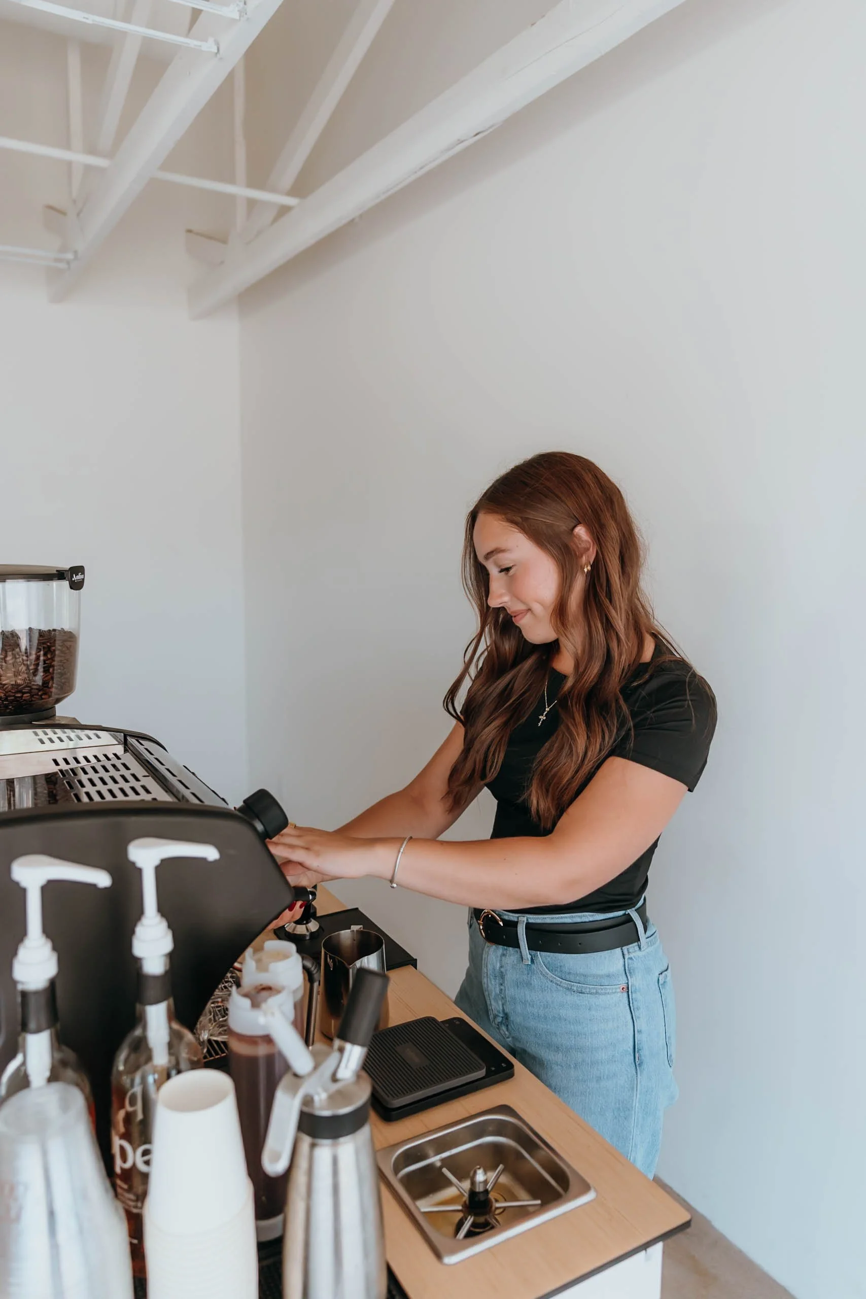 A professional barista preparing beverages with an espresso machine and syrup bottles on the counter.