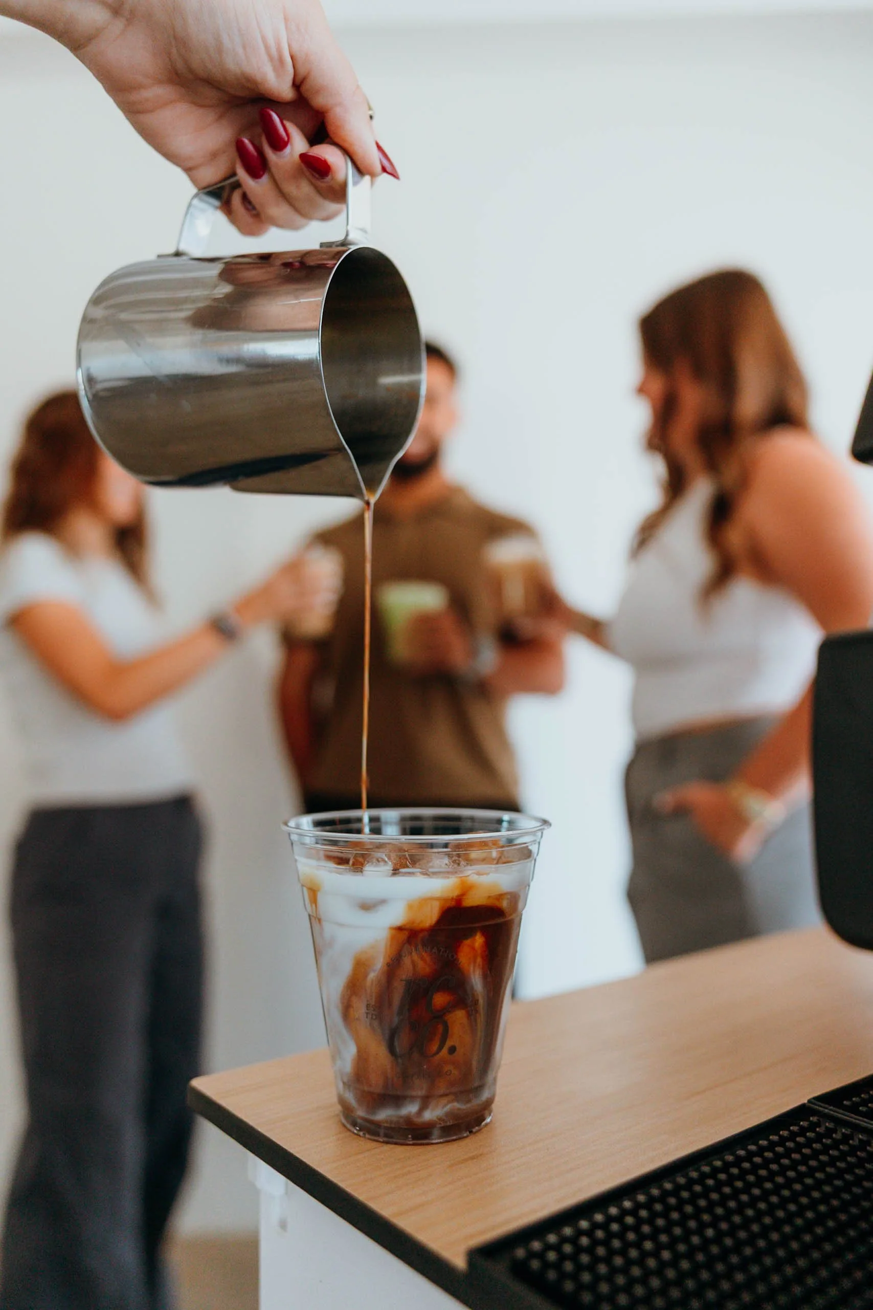 Pouring iced coffee into a clear glass at an event in Phoenix with people in the background