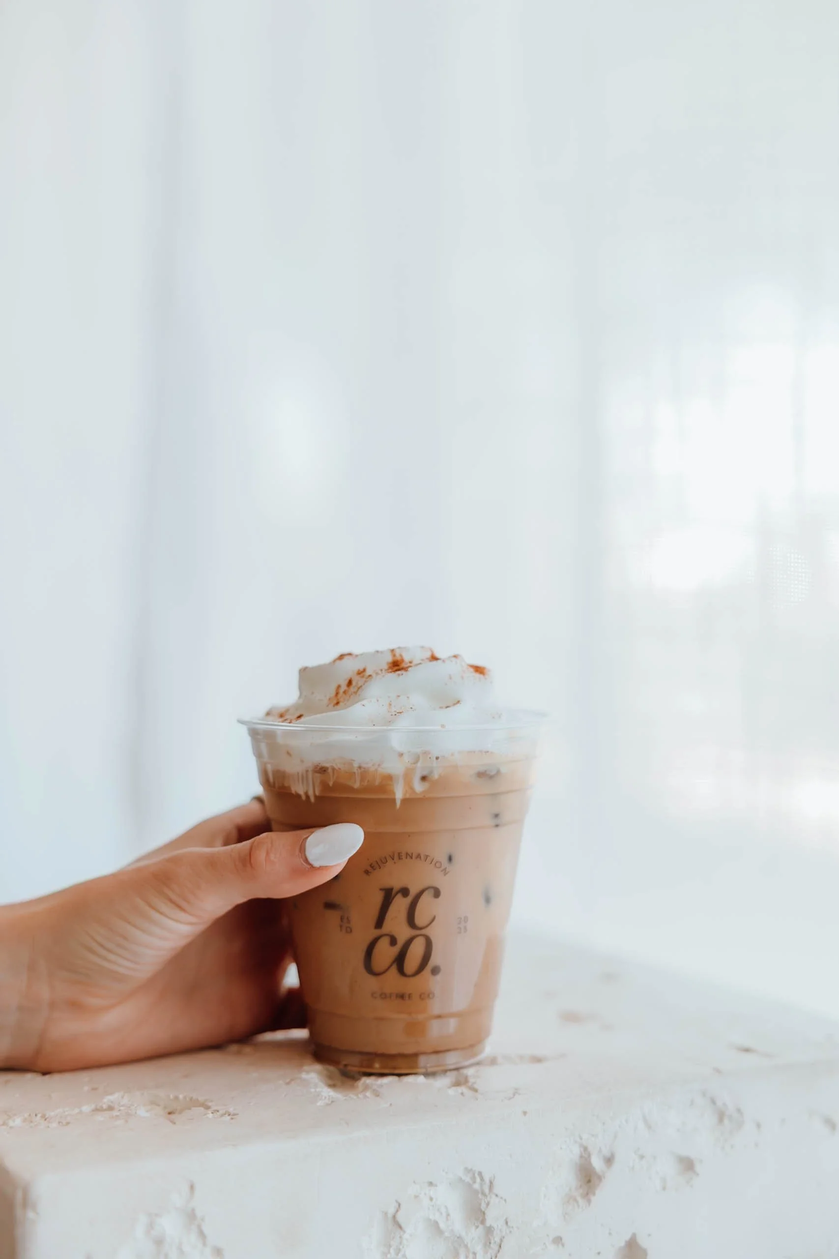 A hand holding a coffee created by Rejuvenation Coffee, a mobile coffee cart for catering services.