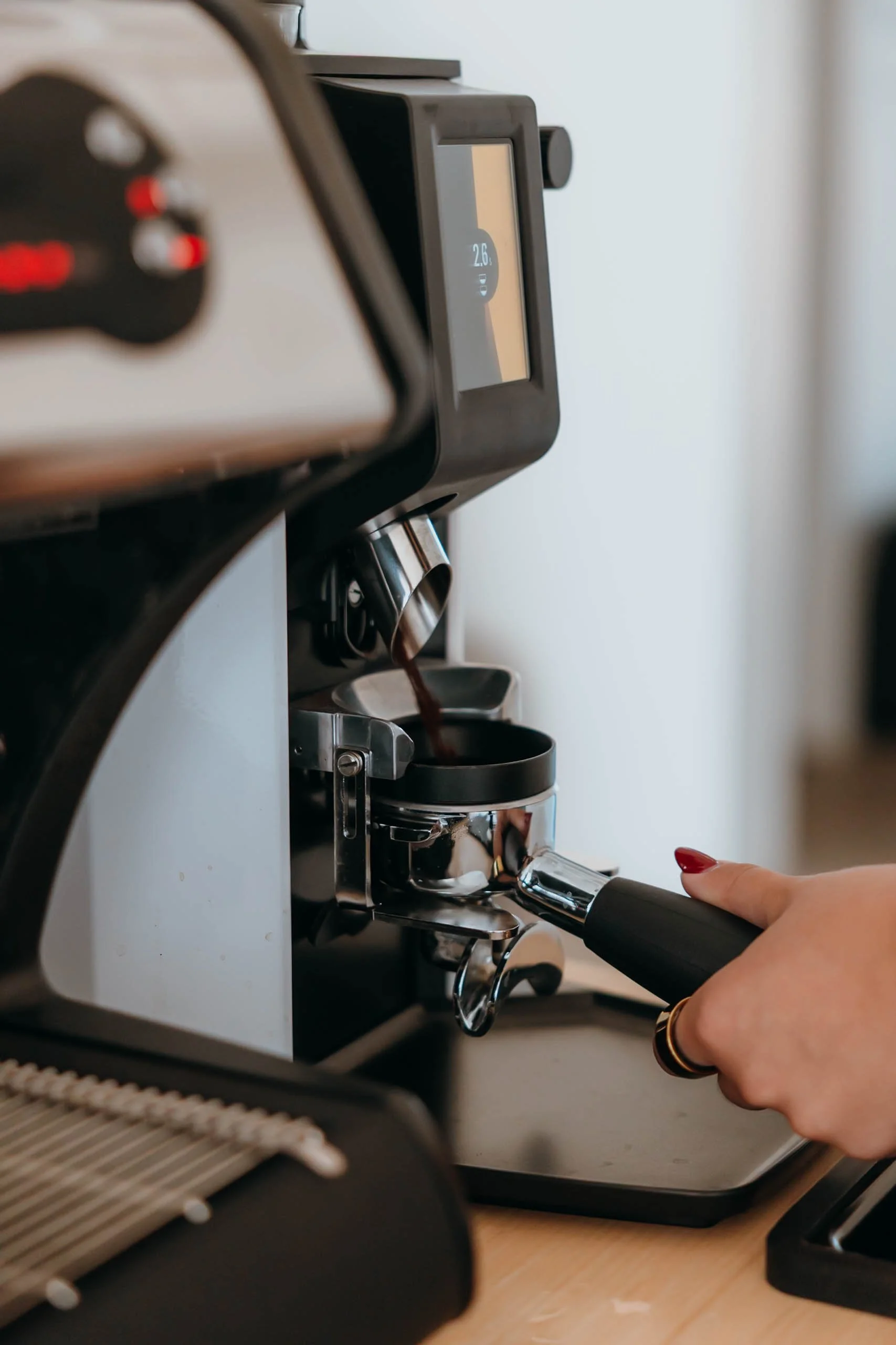 Close-up of a person pressing the portafilter of an espresso machine, with a digital display showing 2.6, in a coffee-making setting.