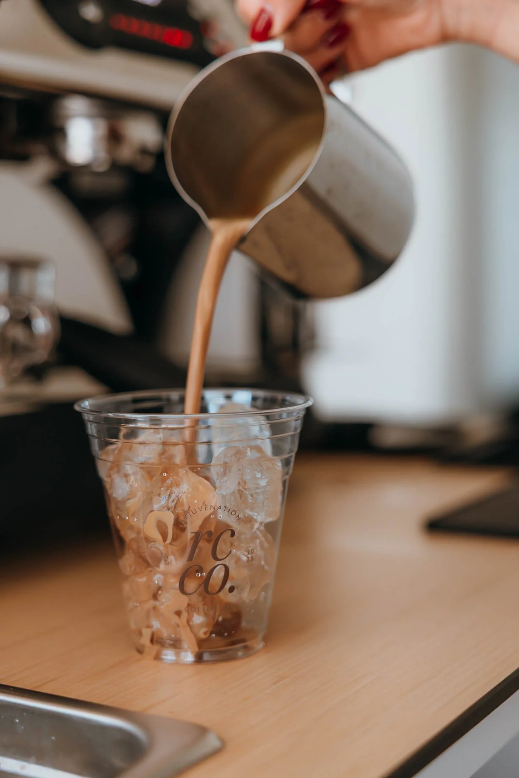 Barista pouring a freshly prepared specialty coffee drink into a Rejuvenation Coffee Co. cup at a catered event.
