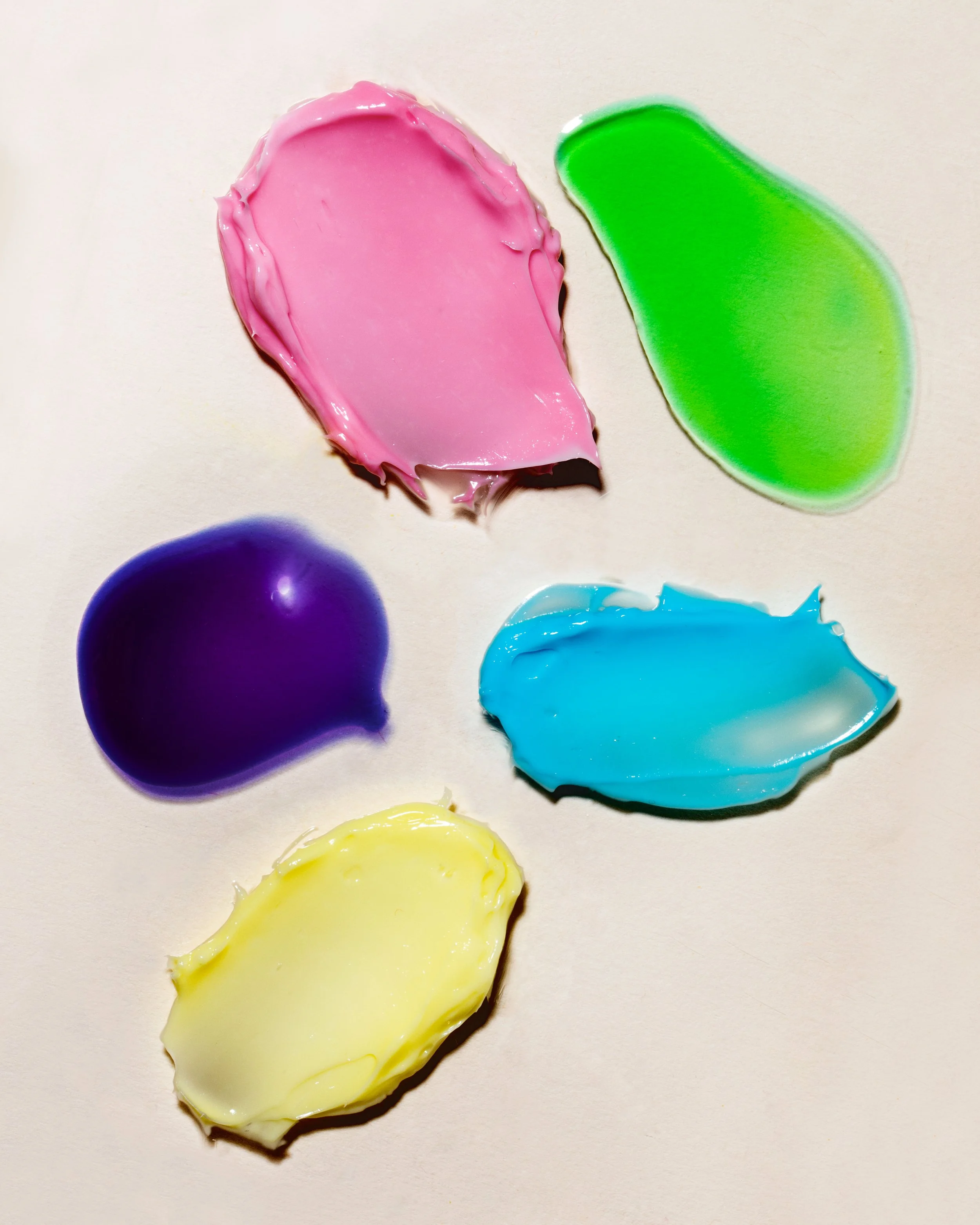 Assorted blobs of colorful paint in pink, green, blue, purple, and yellow on a white surface.