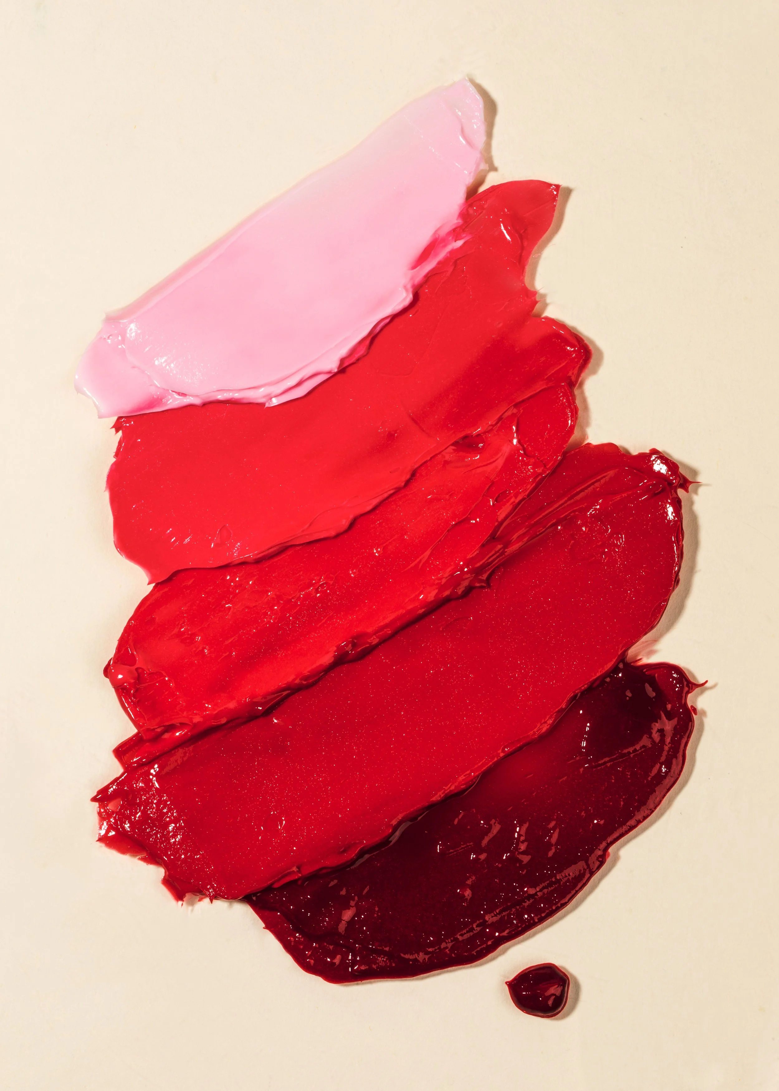 Multiple streaks of different shades of red and pink paint on a white surface.