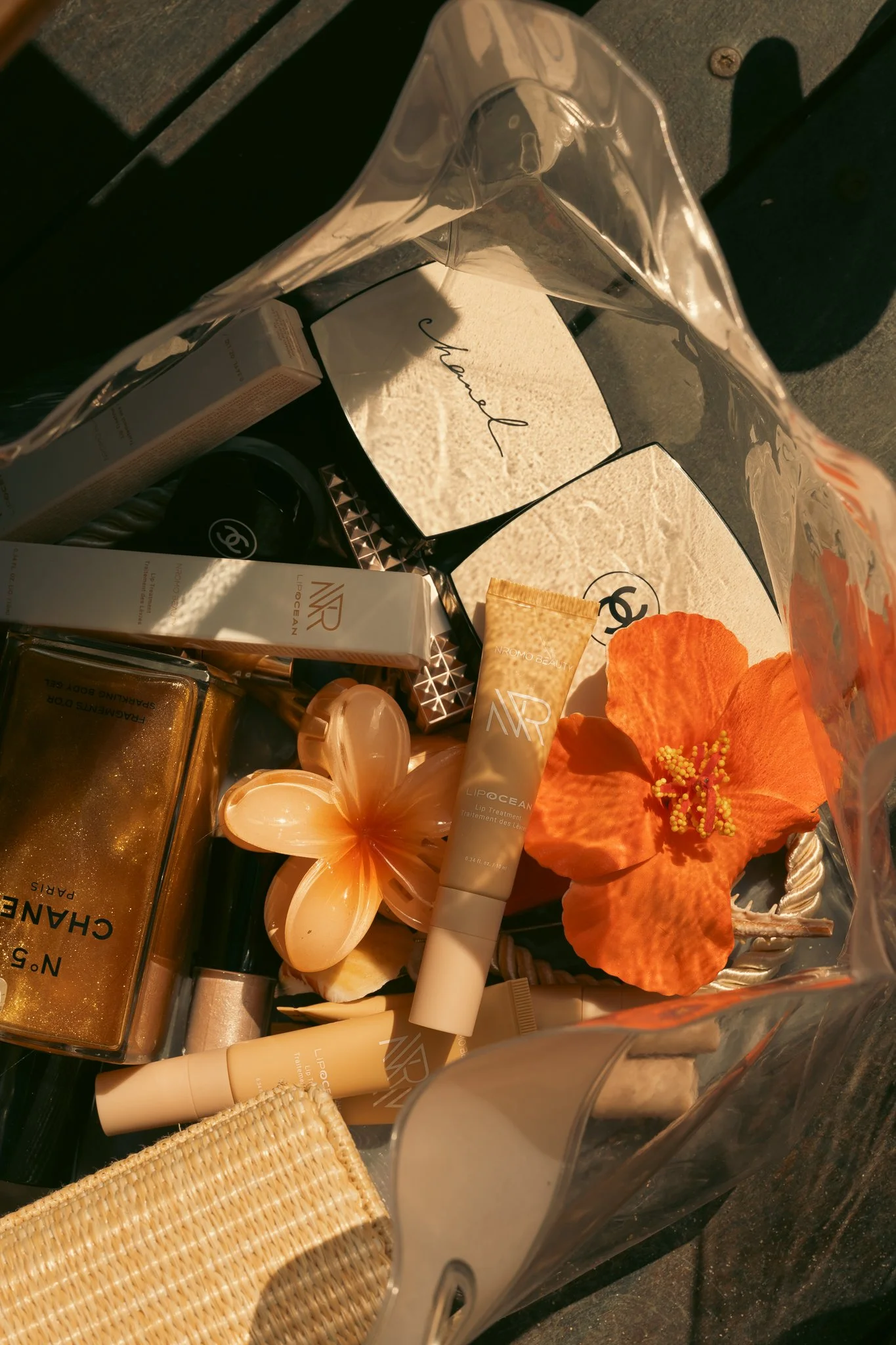 Collection of beauty products inside a transparent gift bag with orange flower and a card in the background.