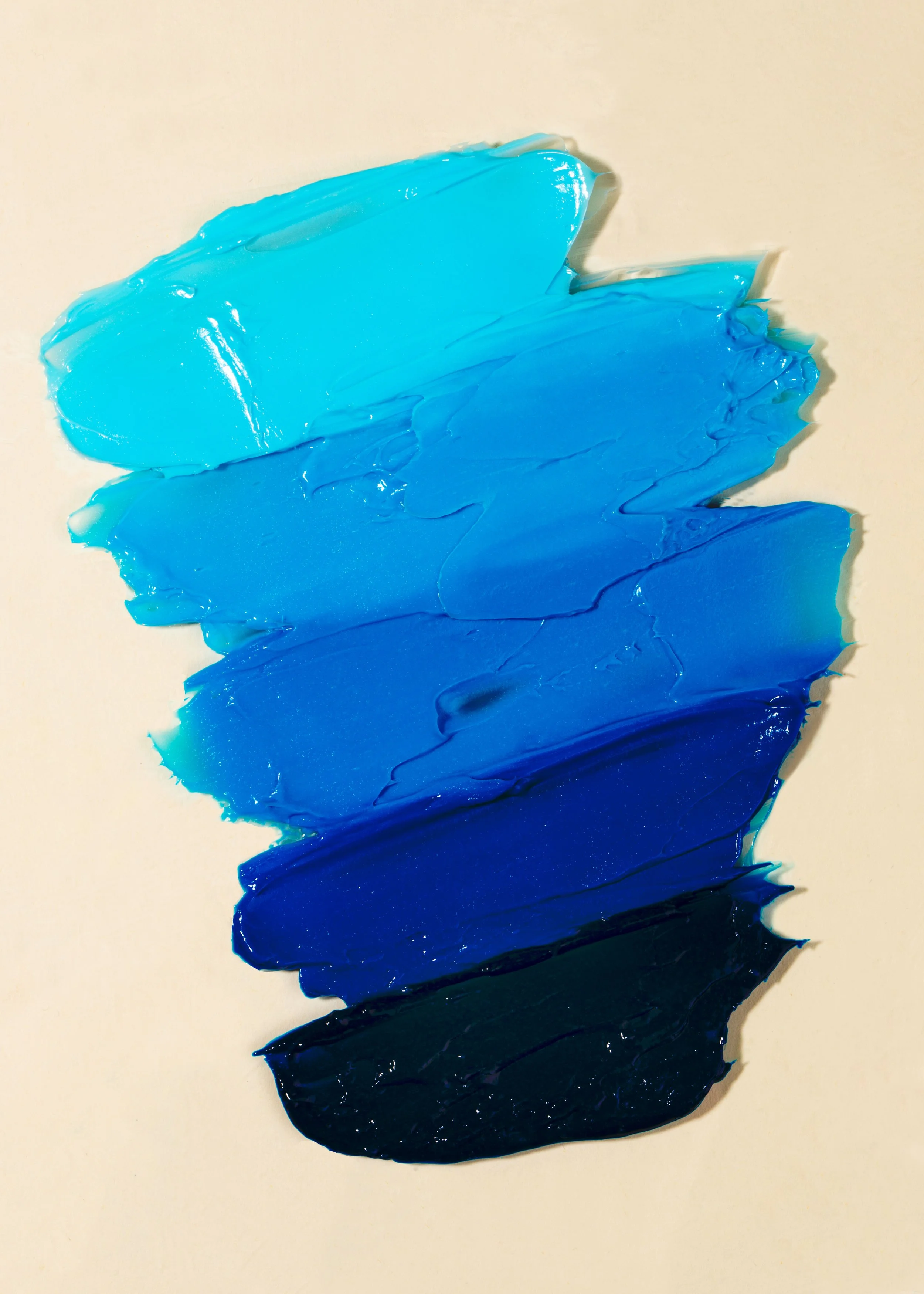 Swatches of various shades of blue and black acrylic paint smeared on a white surface.