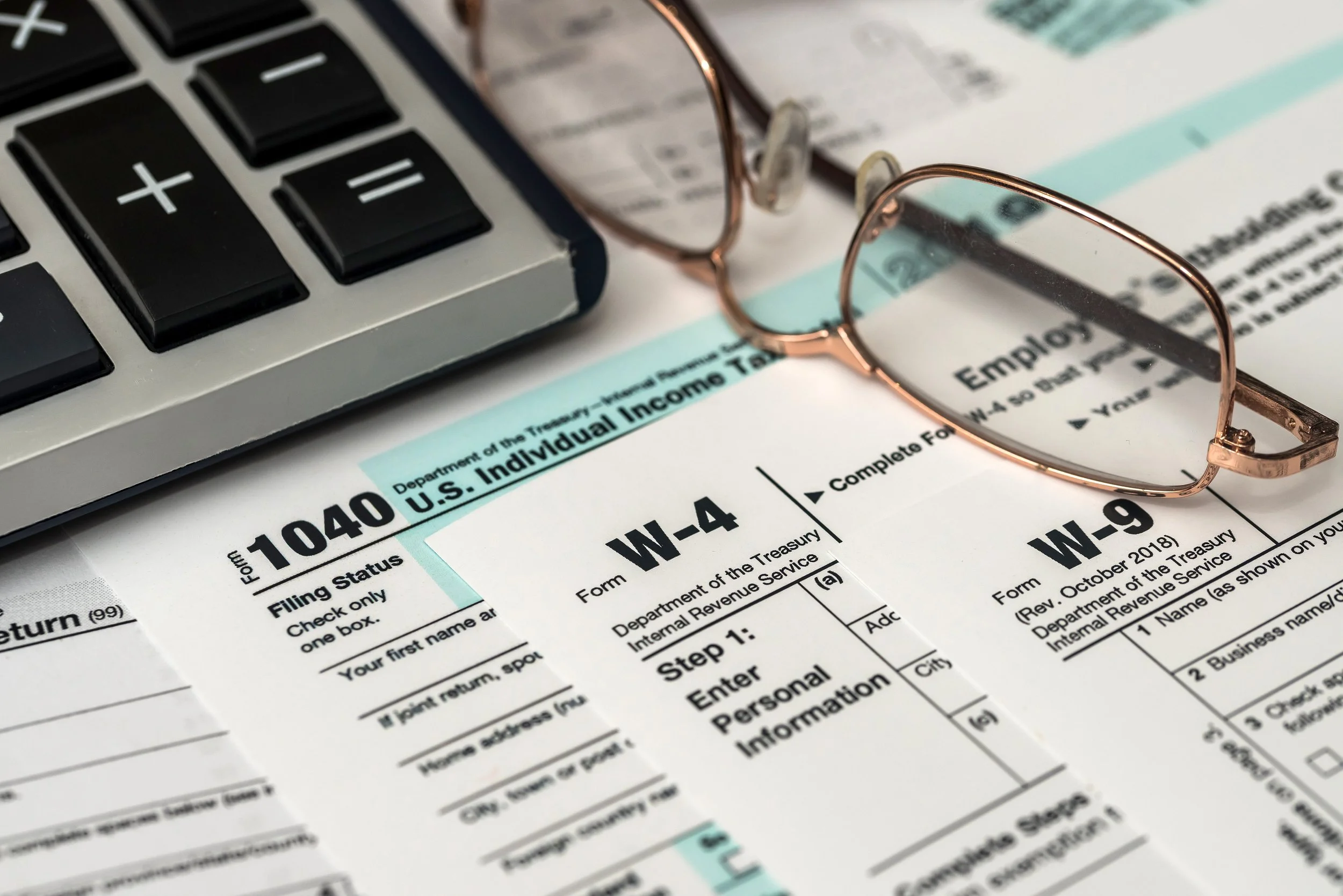 Close-up of a tax form, a pair of pink eyeglasses, a calculator, and a receipt on a desk.