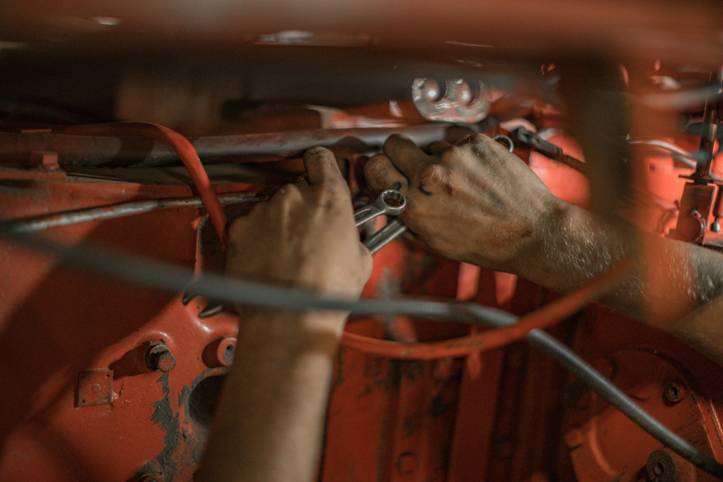 Close-up of a person's hands using a wrench to work on machinery inside a red-orange industrial or mechanical device.