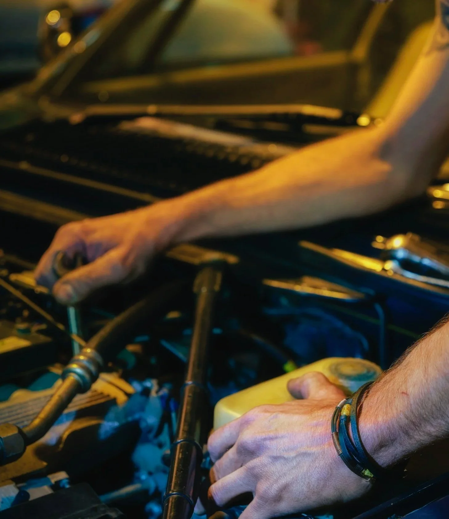 Close-up of a person’s hand working on a metal part in a workshop or garage, with tools and mechanical components surrounding.