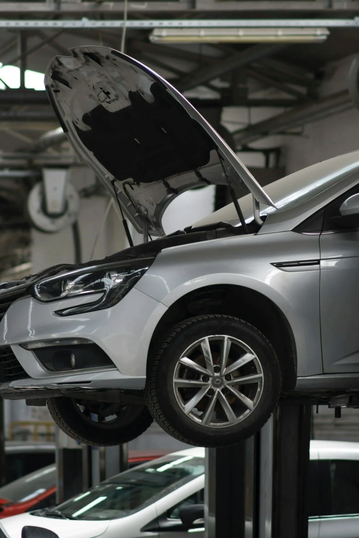 Multiple cars on an assembly line inside an automotive manufacturing plant, with the top car's hood open.
