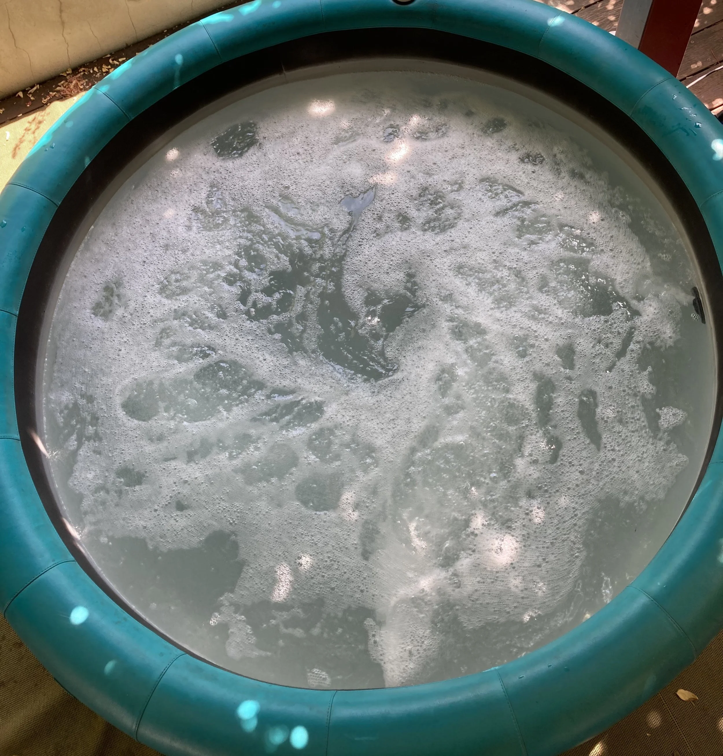 A round small pool filled with water and foam, with a blue-colored rim and sunlight reflections on the water surface.