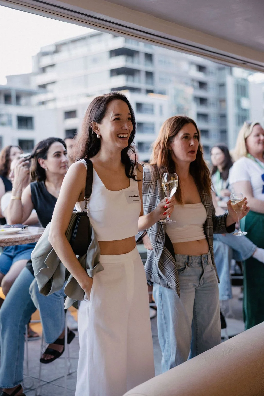 Women attending the Impact Stage launch party, some holding glasses of wine, with modern apartment buildings in the background.