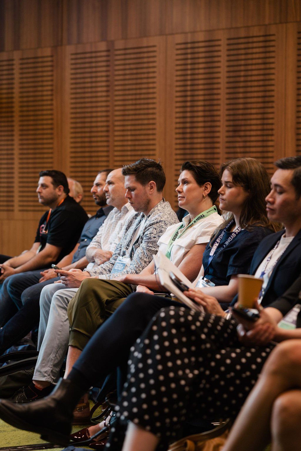 A row of seated conference attendees at the 2025 Impact Stage listening attentively in a room with wooden walls.