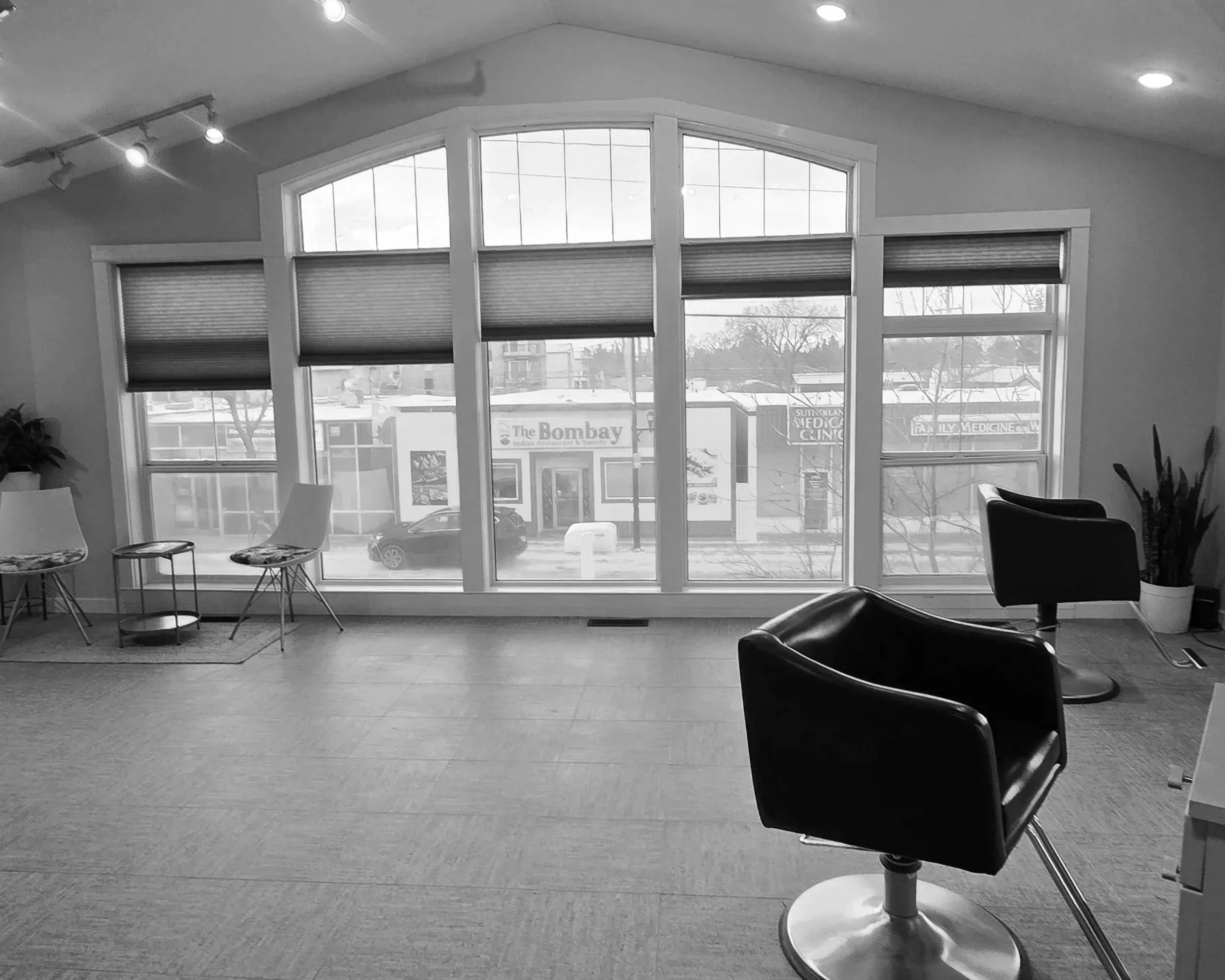 Interior of a hair salon with large windows, two black salon chairs, and additional seating along the wall.