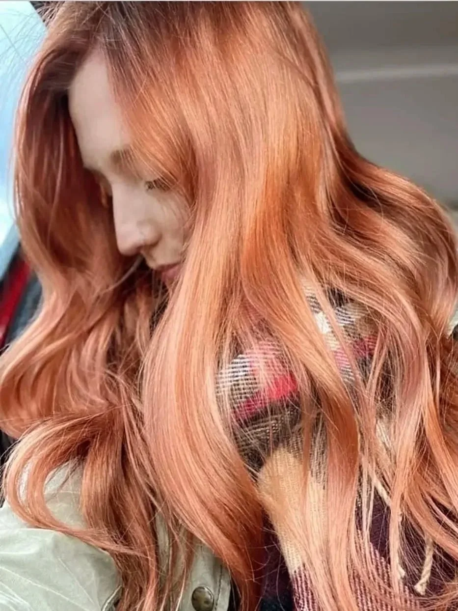 Close-up of a woman with long, wavy, reddish-blonde hair, looking downward.