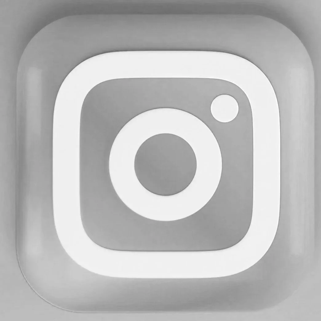 Black and white icon of the Instagram logo with a rounded square and a small circle in the top right corner.