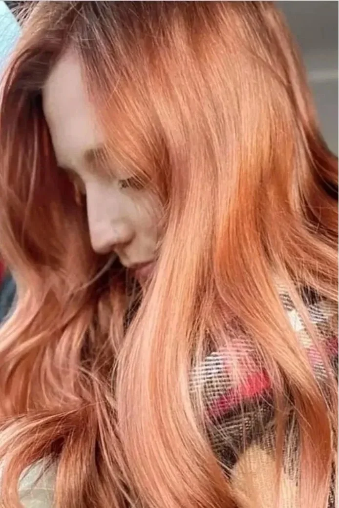 A woman with long, wavy, reddish hair looking down.