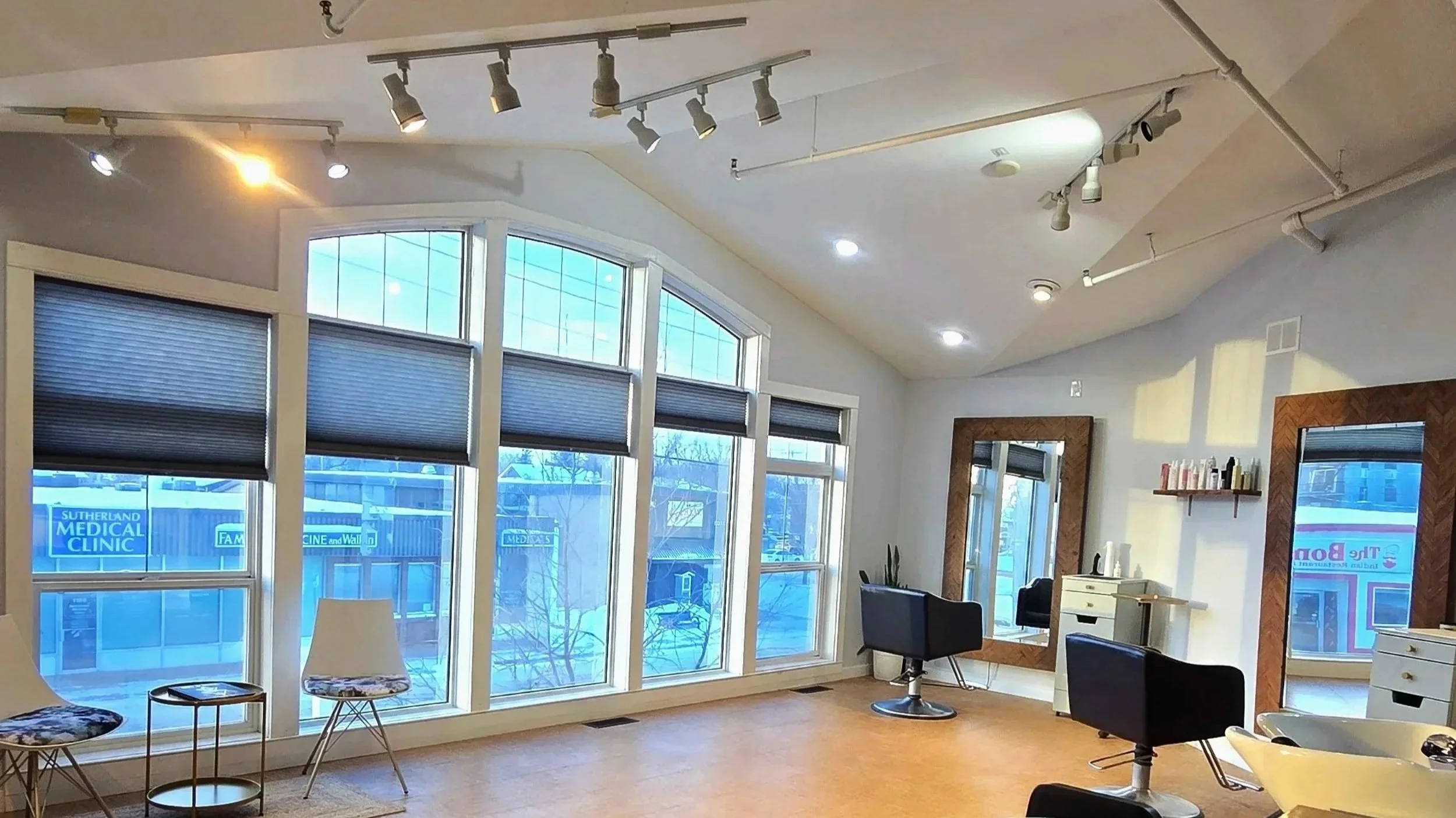 Stylish hair salon with large windows, black salon chairs, mirrors, and hair care products on shelves.