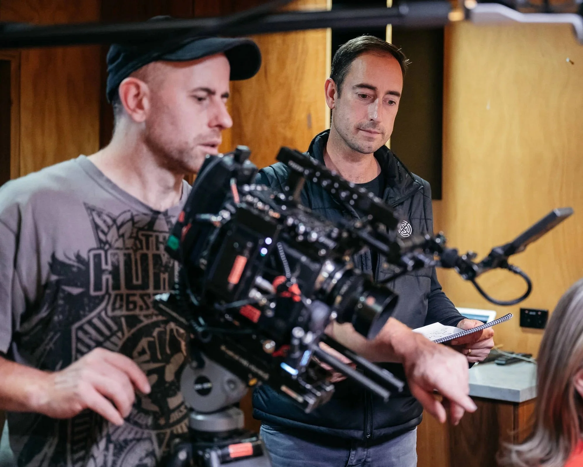Two men looking at a camera equipment and a notebook in an indoor setting with wooden wall panels.