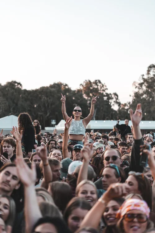 women sitting on shoulders in a crowd who are signing, smiling and dancing at a music festival in McLaren Vale, South Australia