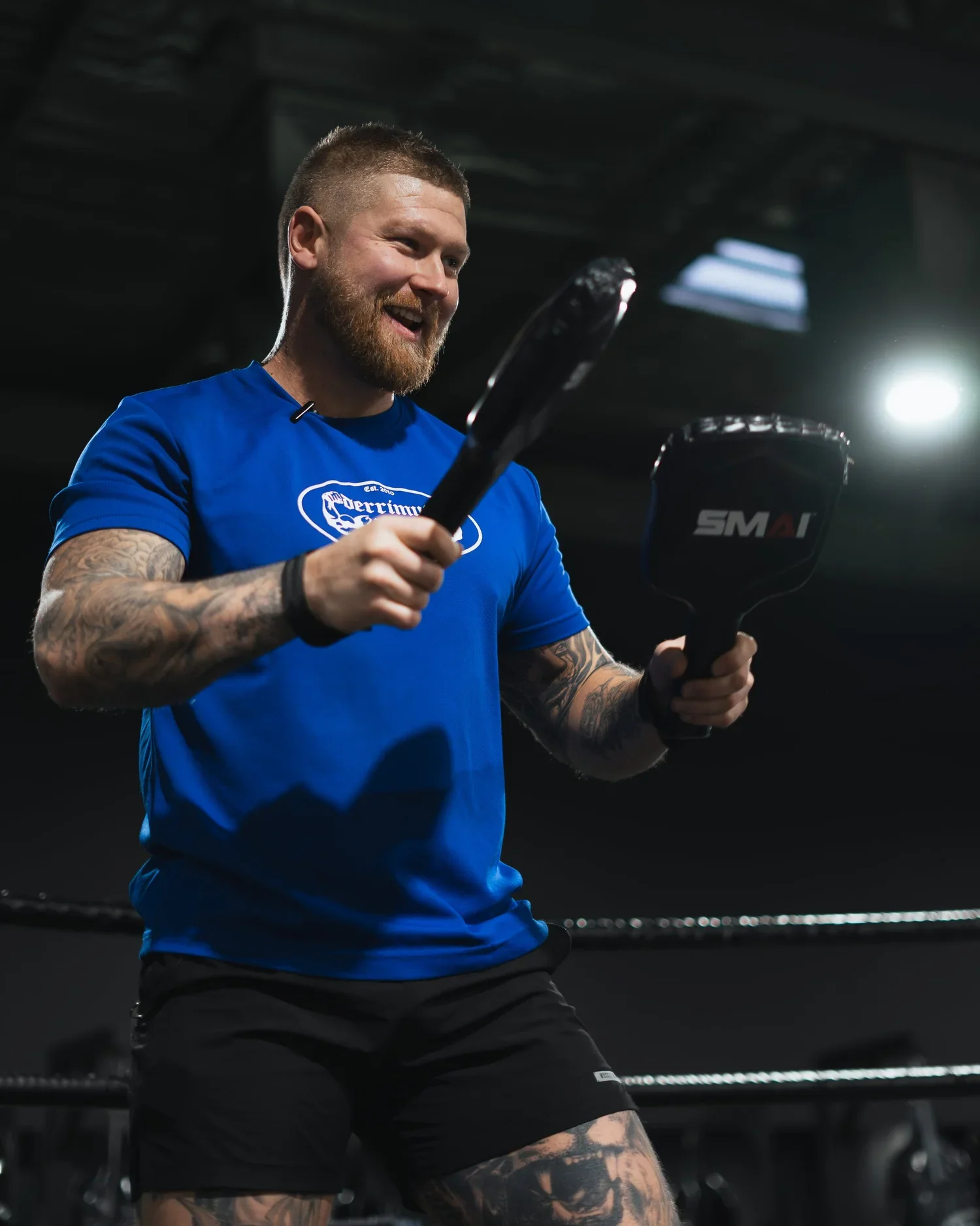 a male personal trainer smiling while holding boxing equipment
