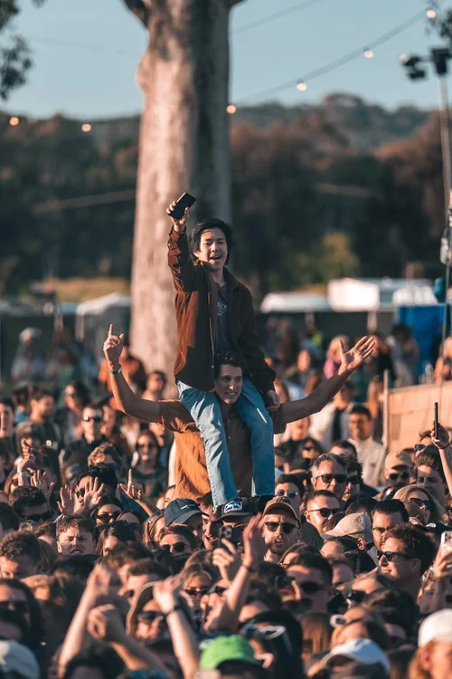 women sitting on shoulders in a crowd who are signing, smiling and dancing at a music festival in McLaren Vale, South Australia