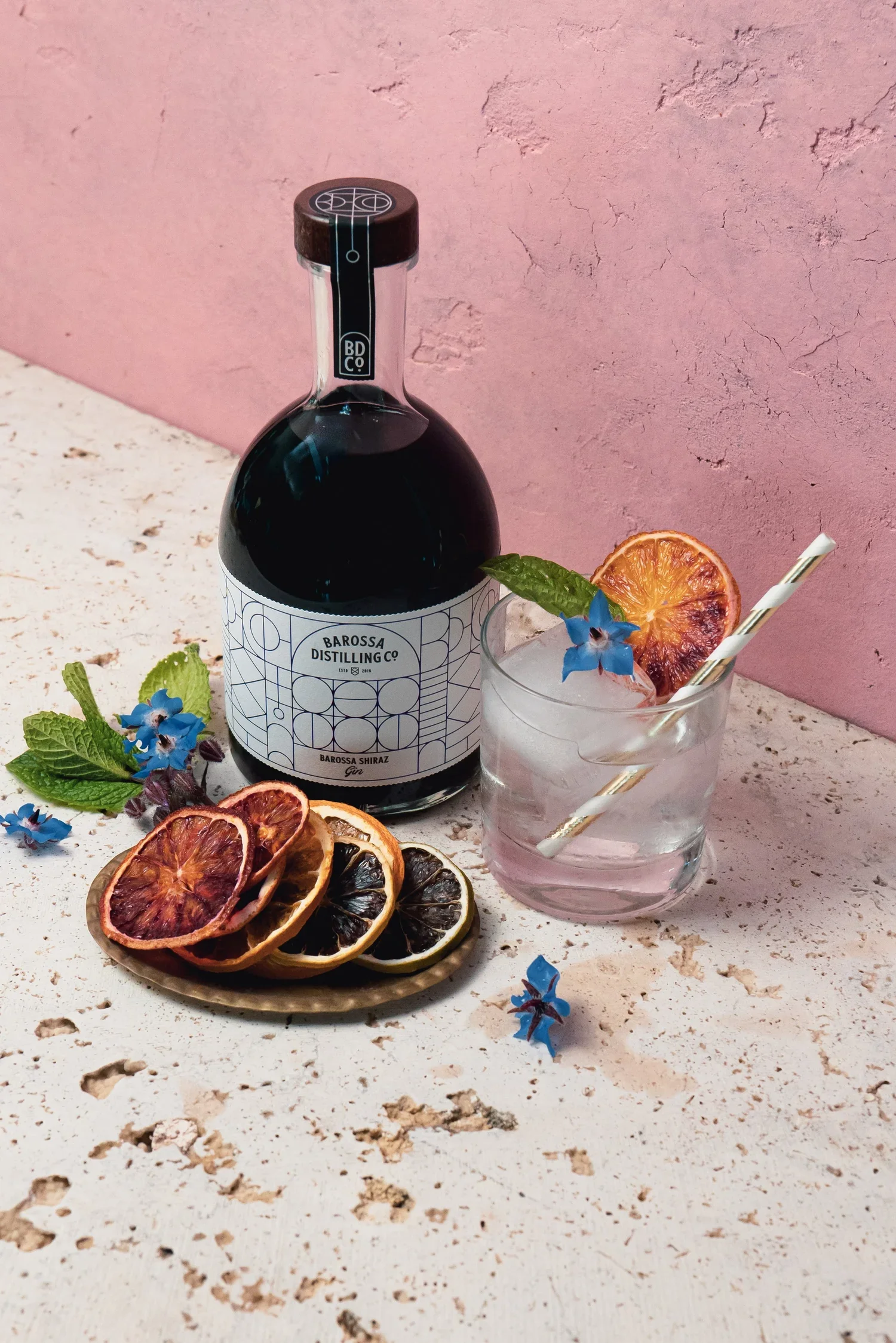 a bottle of shiraz gin and a glass of gin with a straw and dried fruit