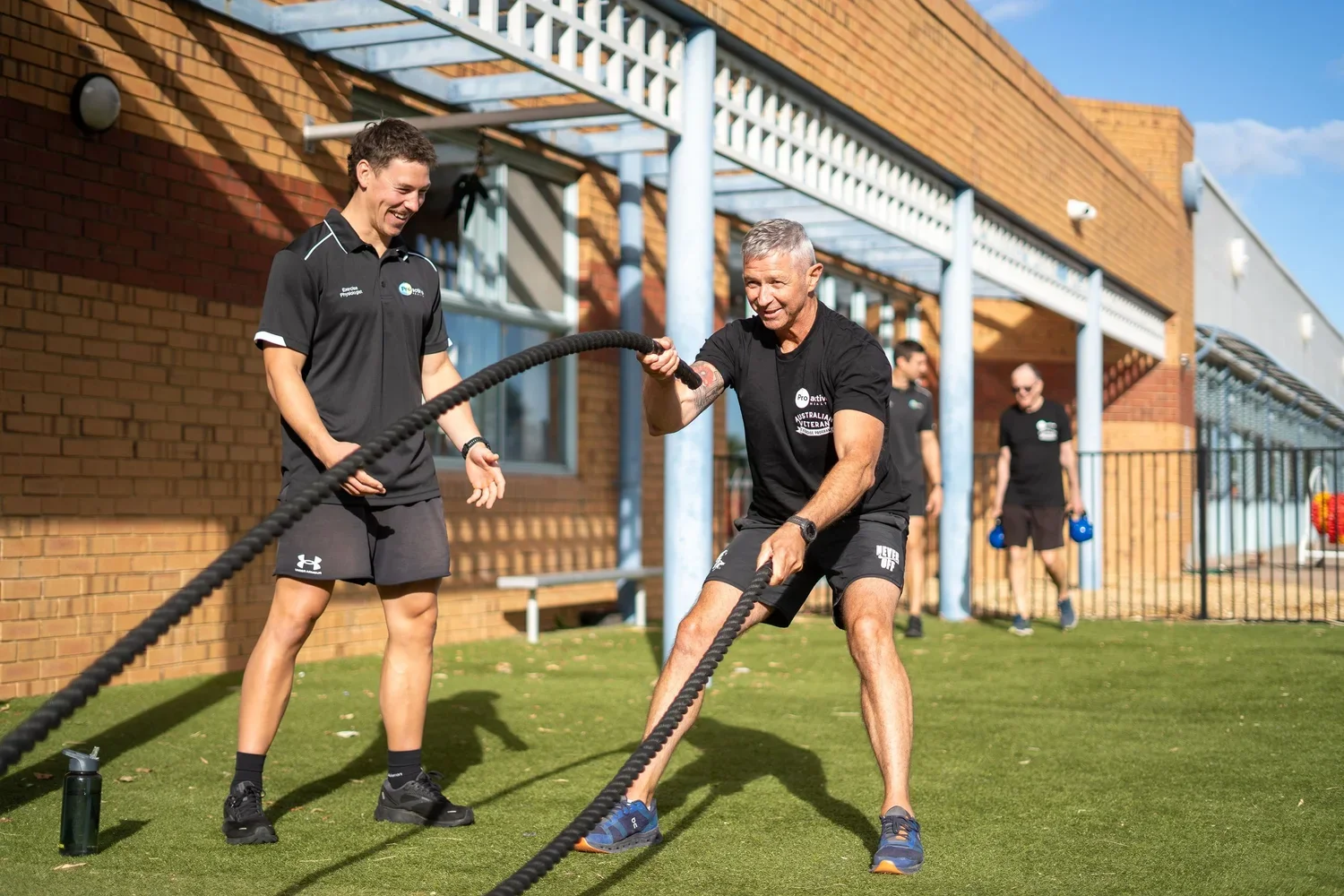 a male personal trainer encourage his male client as he does battle ropes
