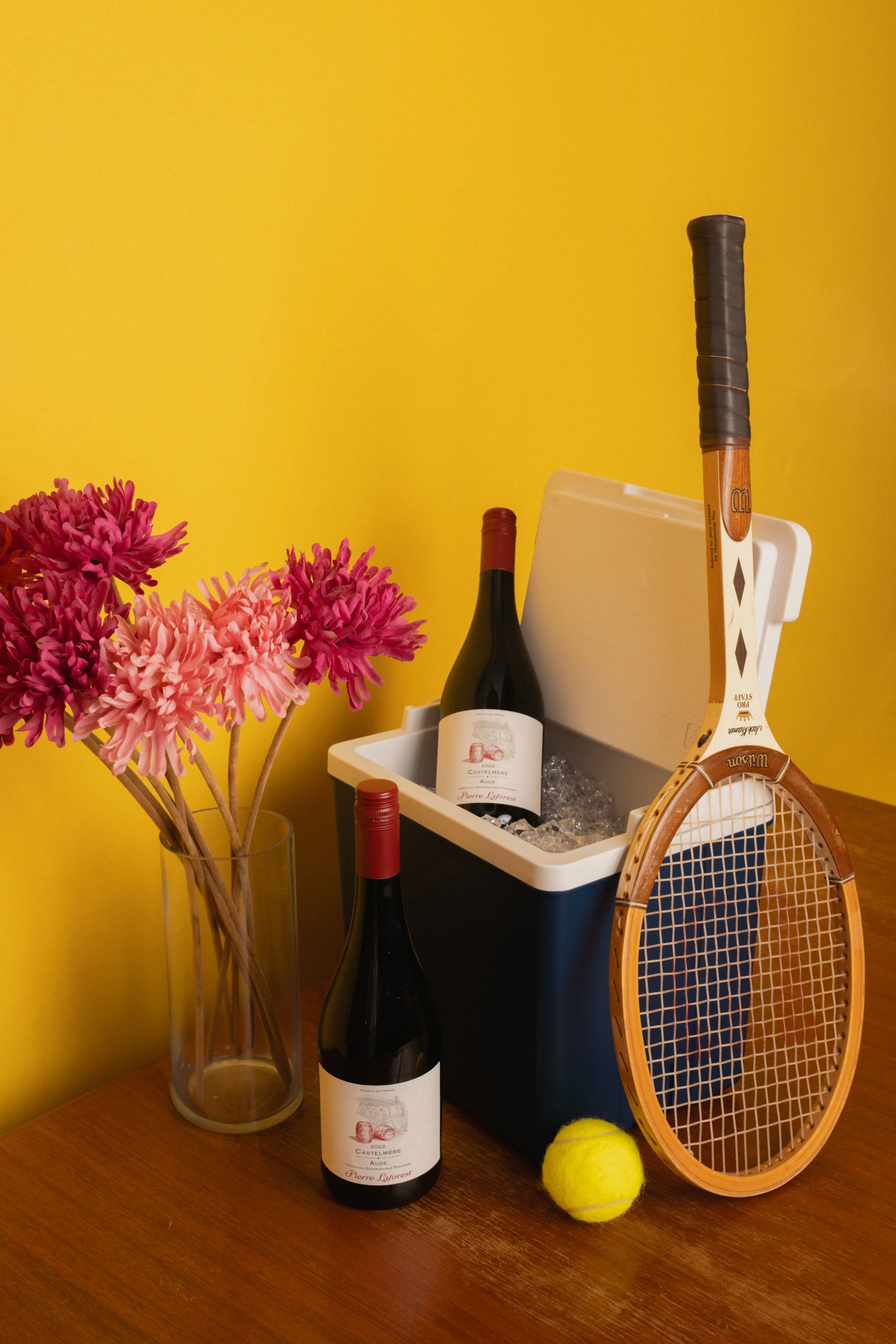 promotional photo of a bottle of wine with a tennis racket and flowers
