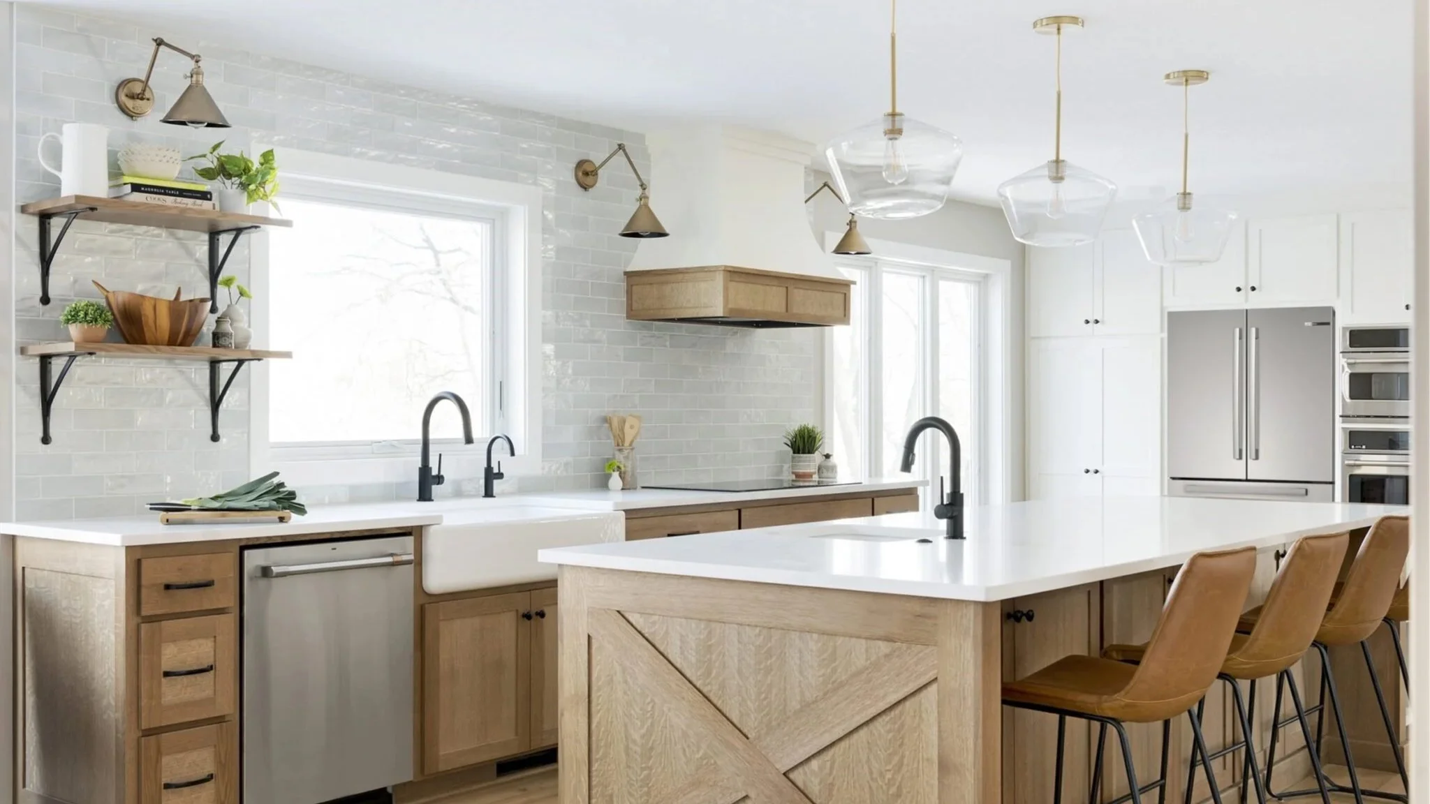 Modern kitchen with white countertops, wooden cabinets, black sink fixtures, brick backsplash, open shelving with plants and dishes, large window, stainless steel appliances, pendant lights, and bar stools.