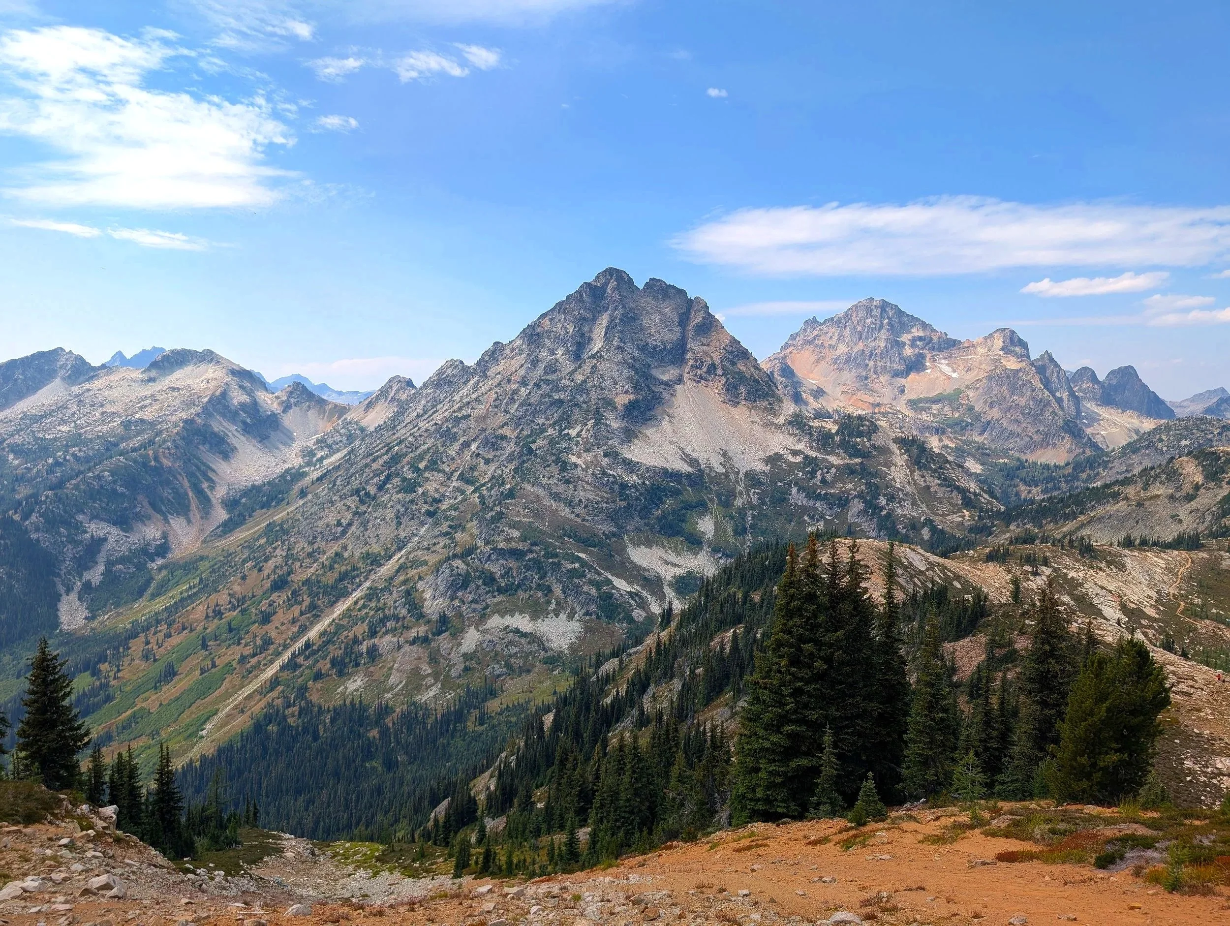 Scenic view of rugged mountains with rocky peaks, green forests, and a blue sky with some clouds.