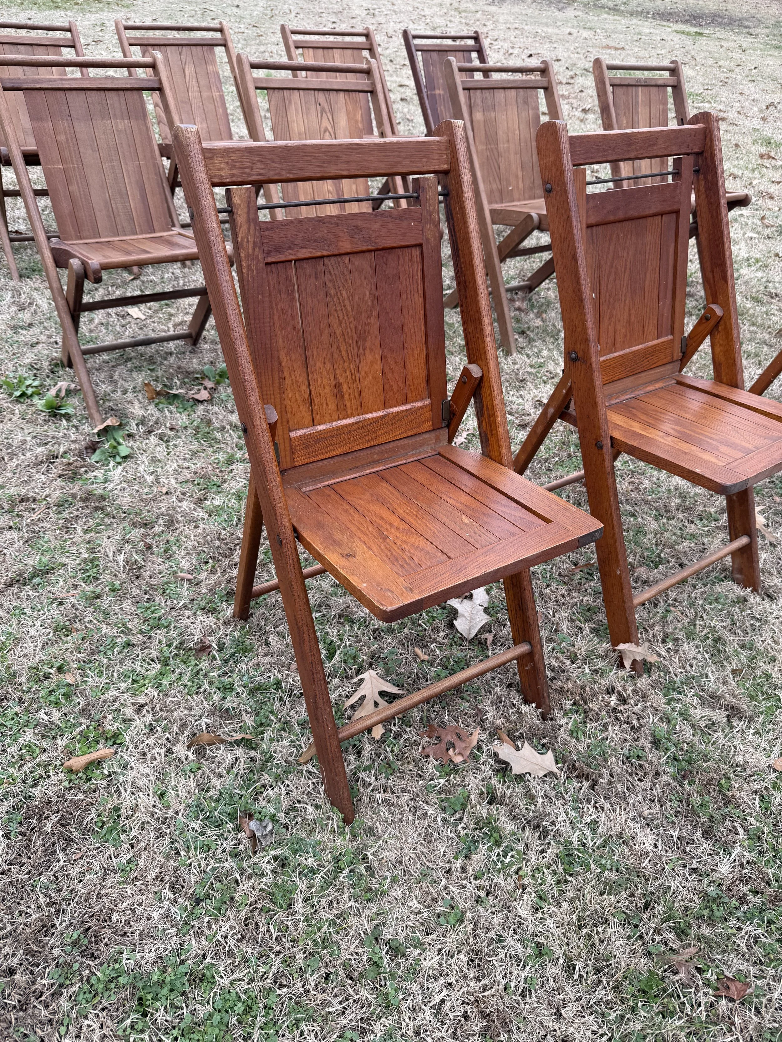 Multiple wooden folding chairs arranged outdoors on a grassy area.