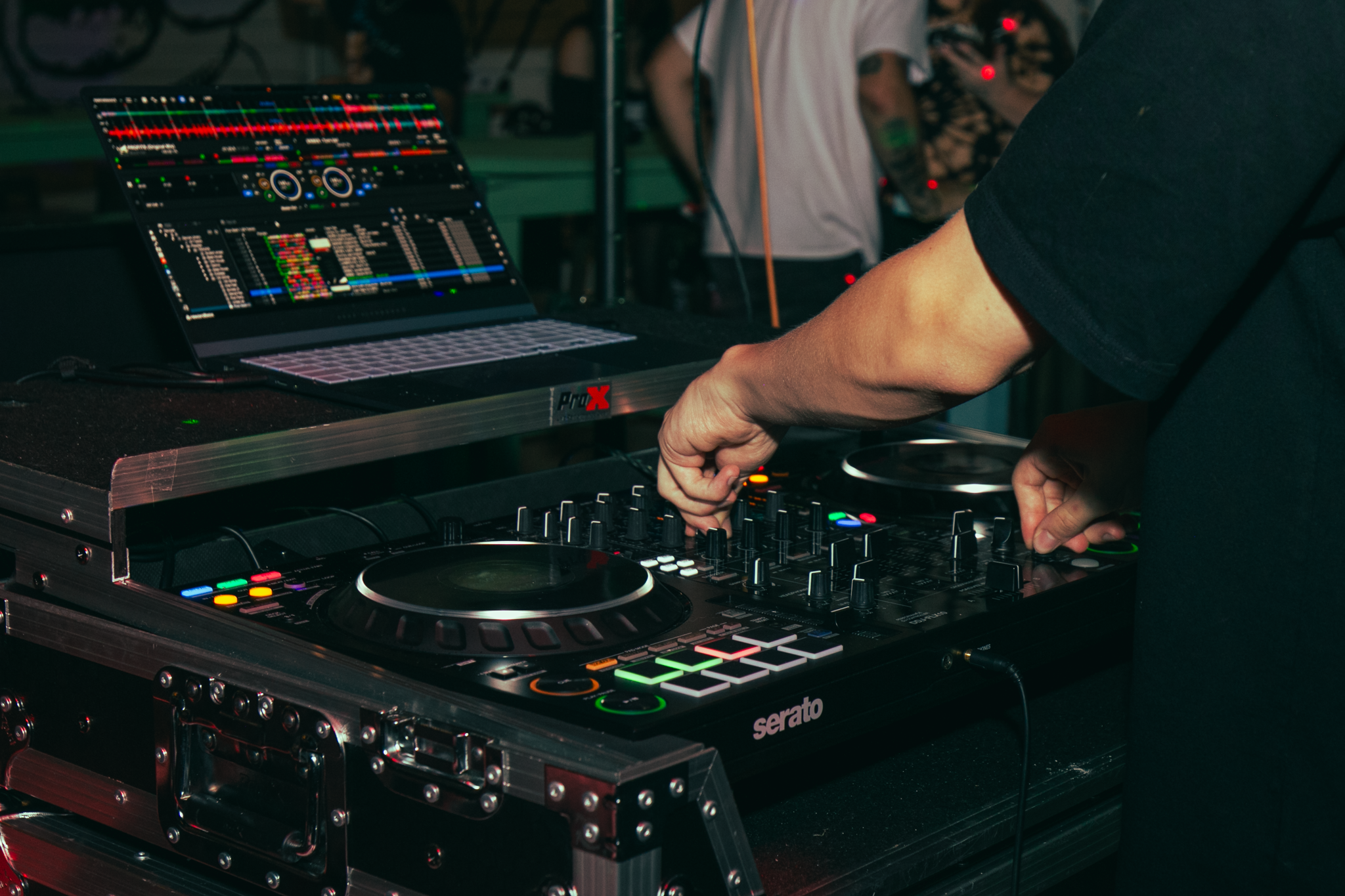 DJ mixing music with a Serato controller at a party or club, with a laptop displaying DJ software in the background.