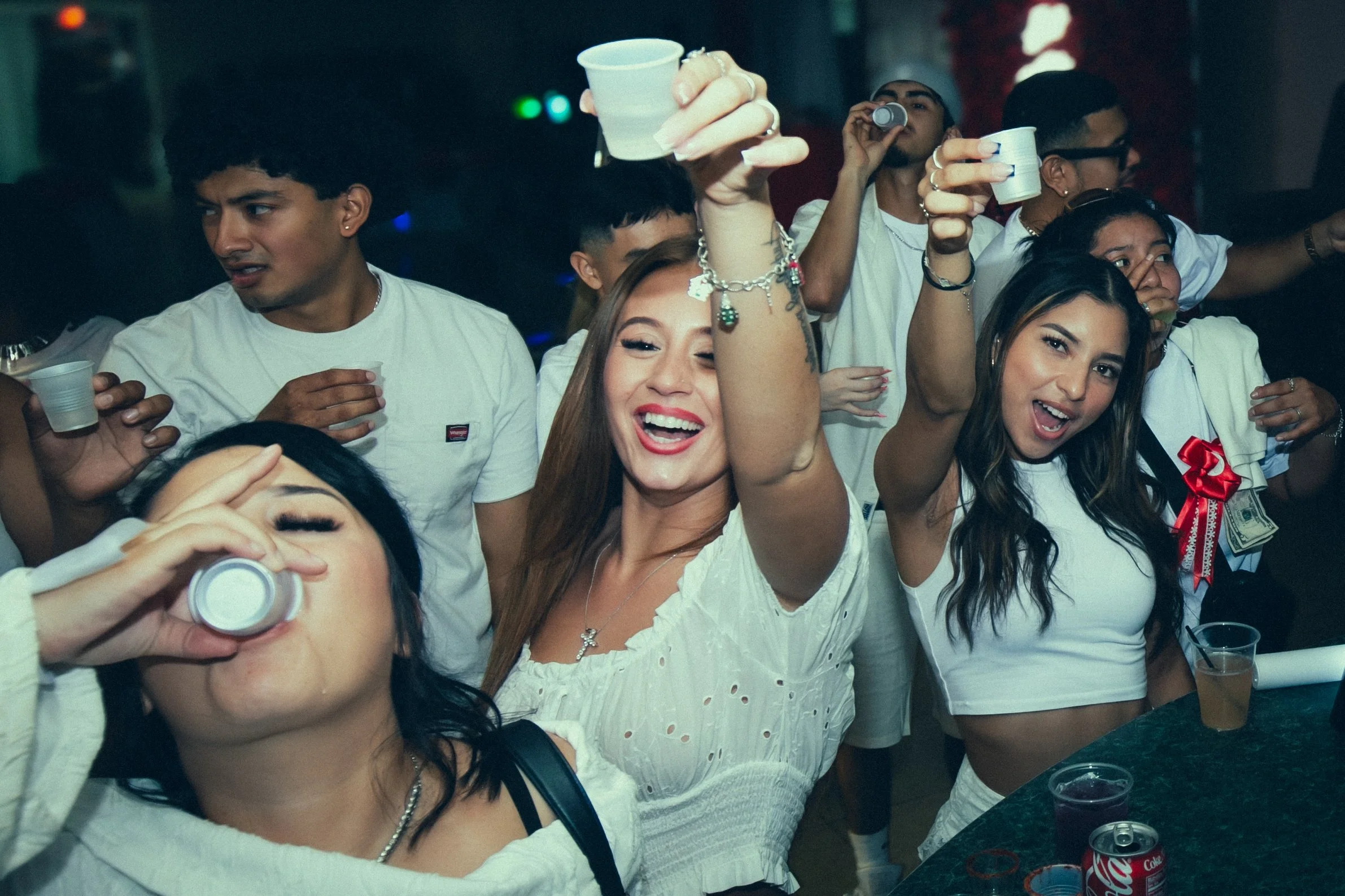 Group of young people celebrating at a party, some holding cups and drinking, smiling and having fun.